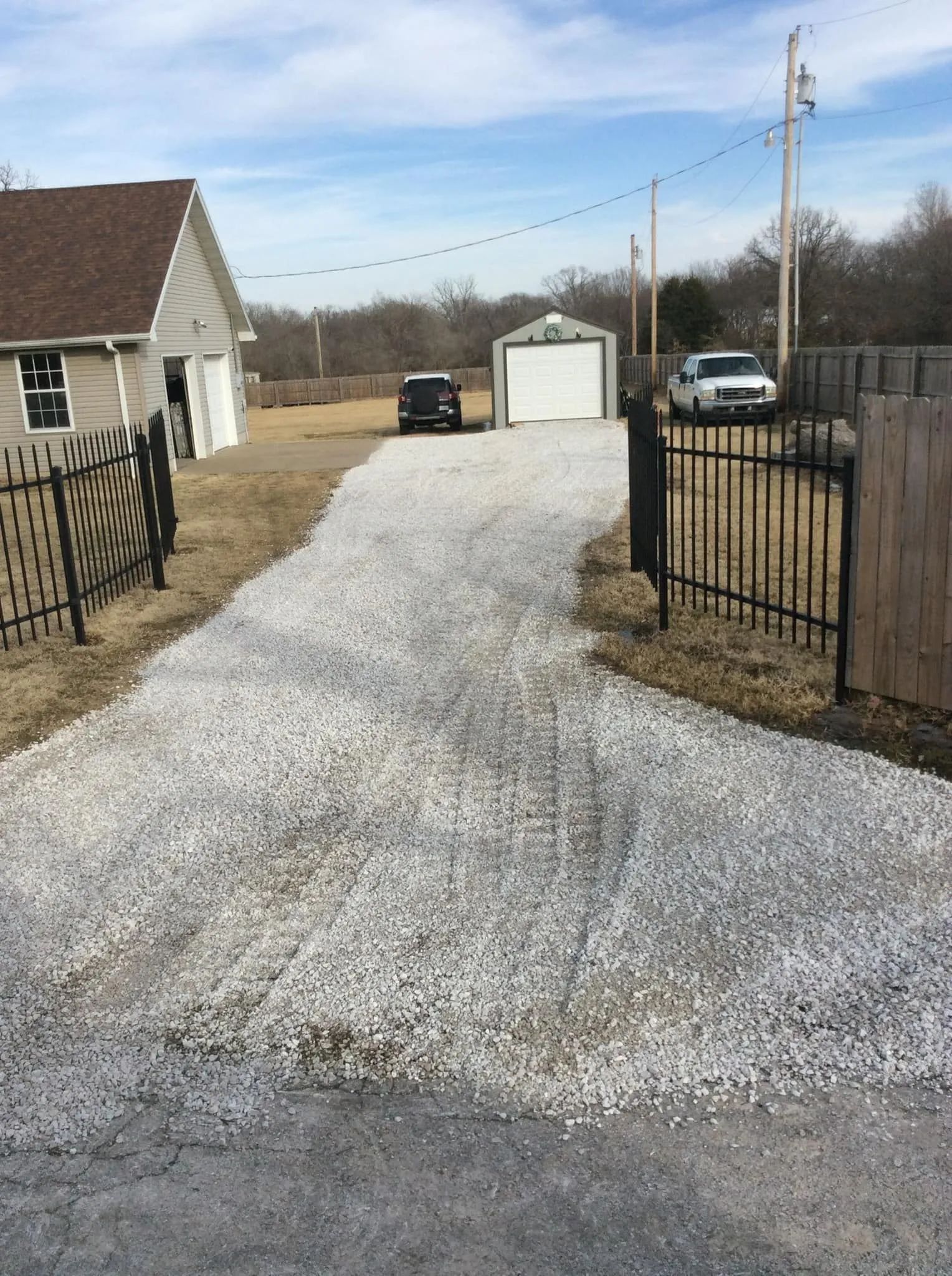 Gravel driveway leading to a garage and parked cars beside a house on a cloudy day