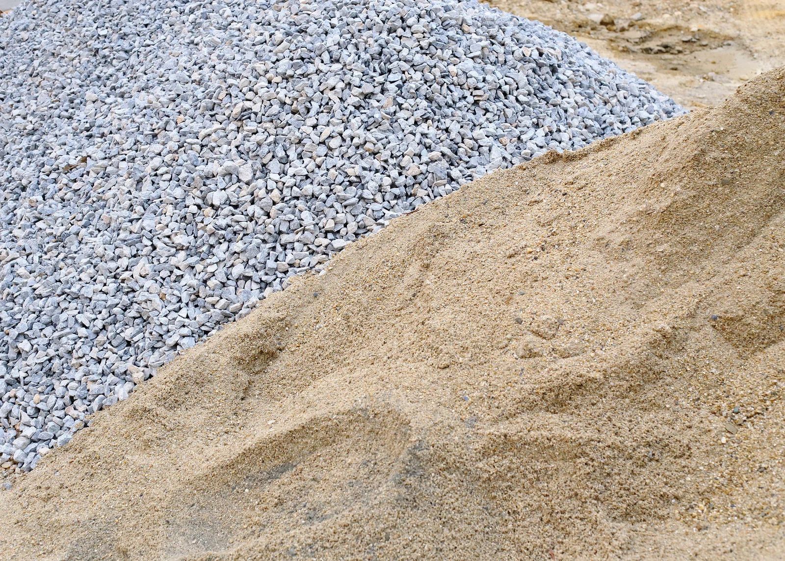 Piles of blue-gray gravel and tan sand stacked in a construction area
