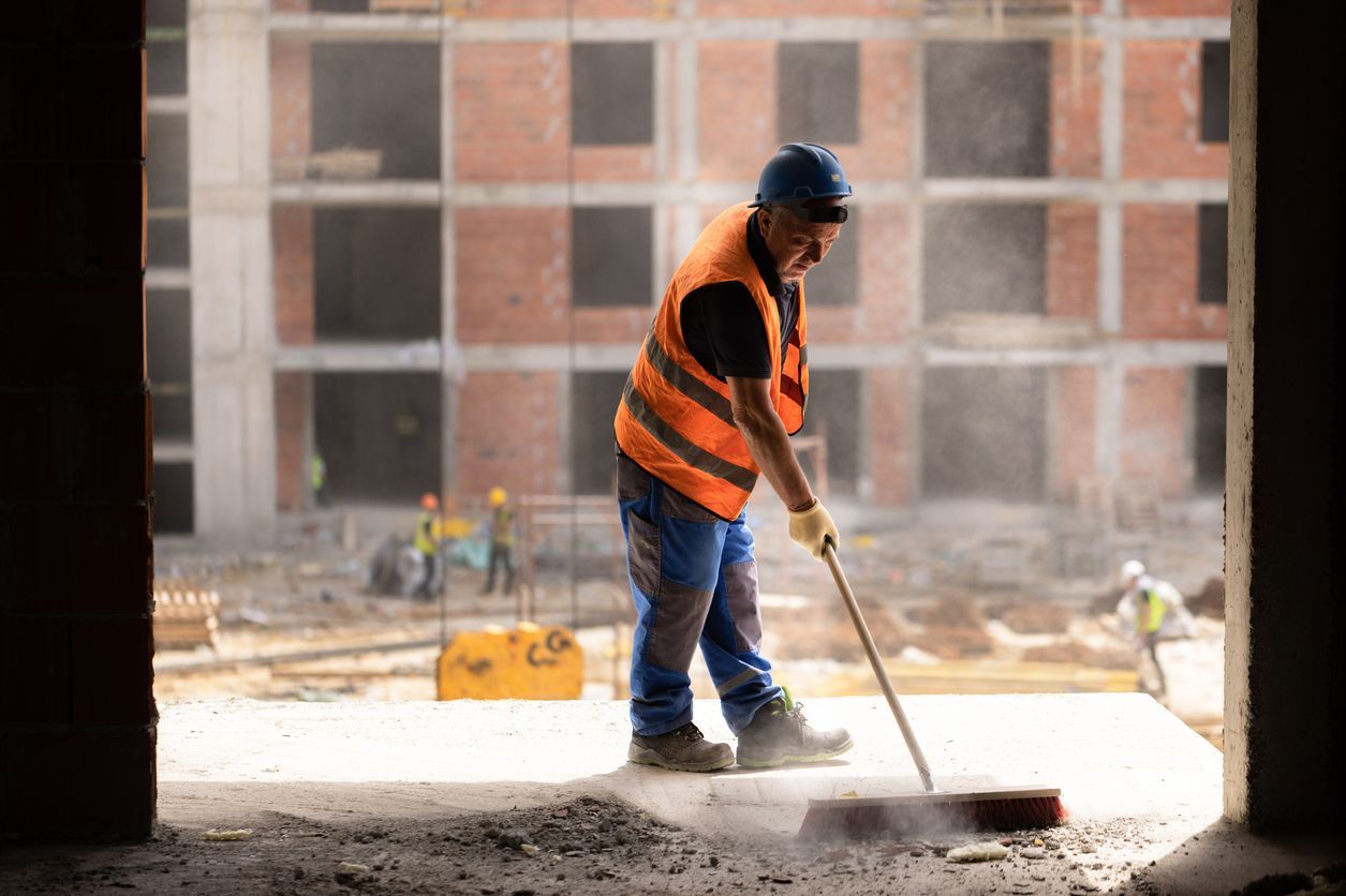 Construction worker in a hard hat and safety vest sweeping debris on a building site.
