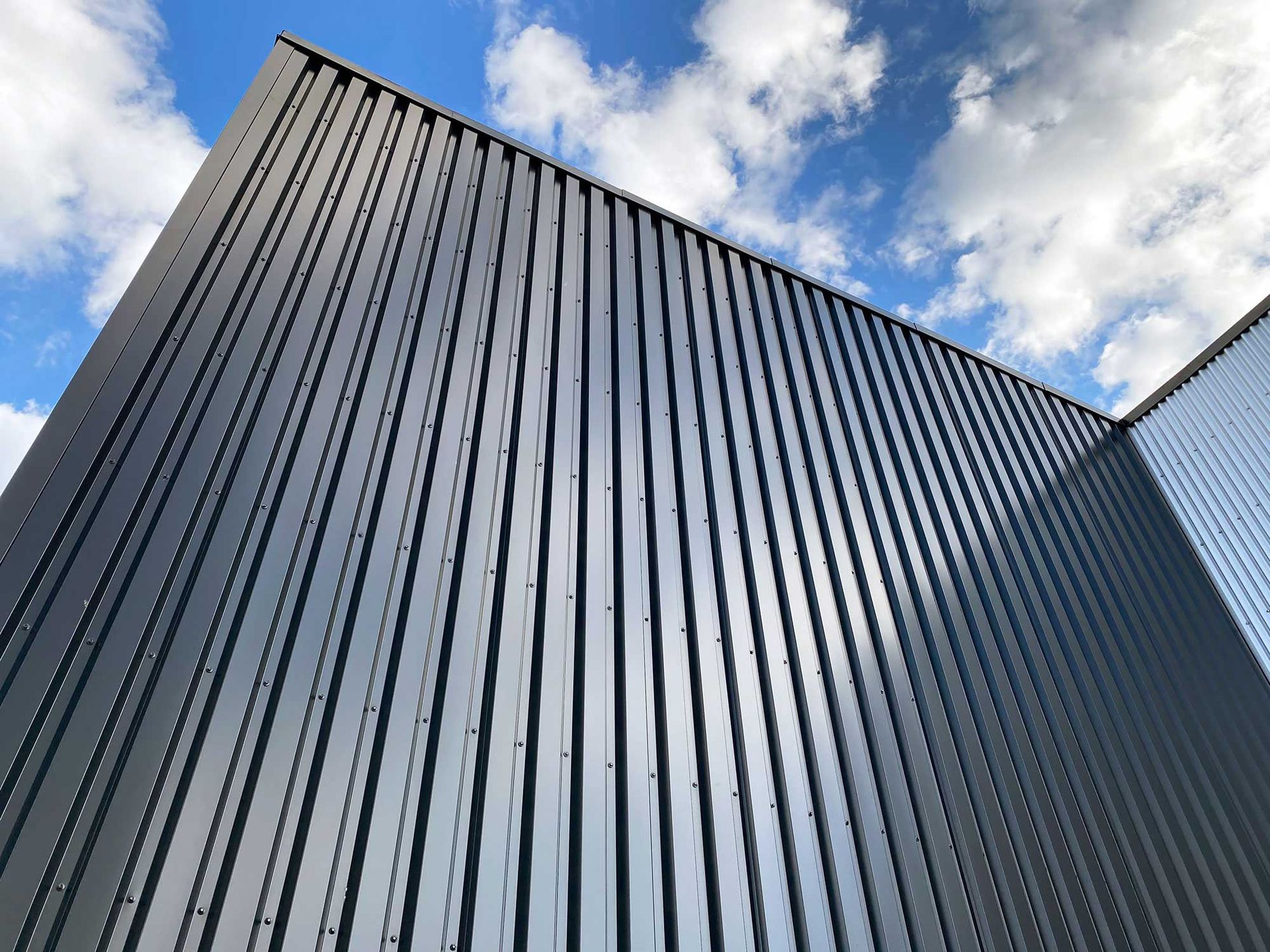 Upward view of a tall corrugated metal building against a blue sky with clouds