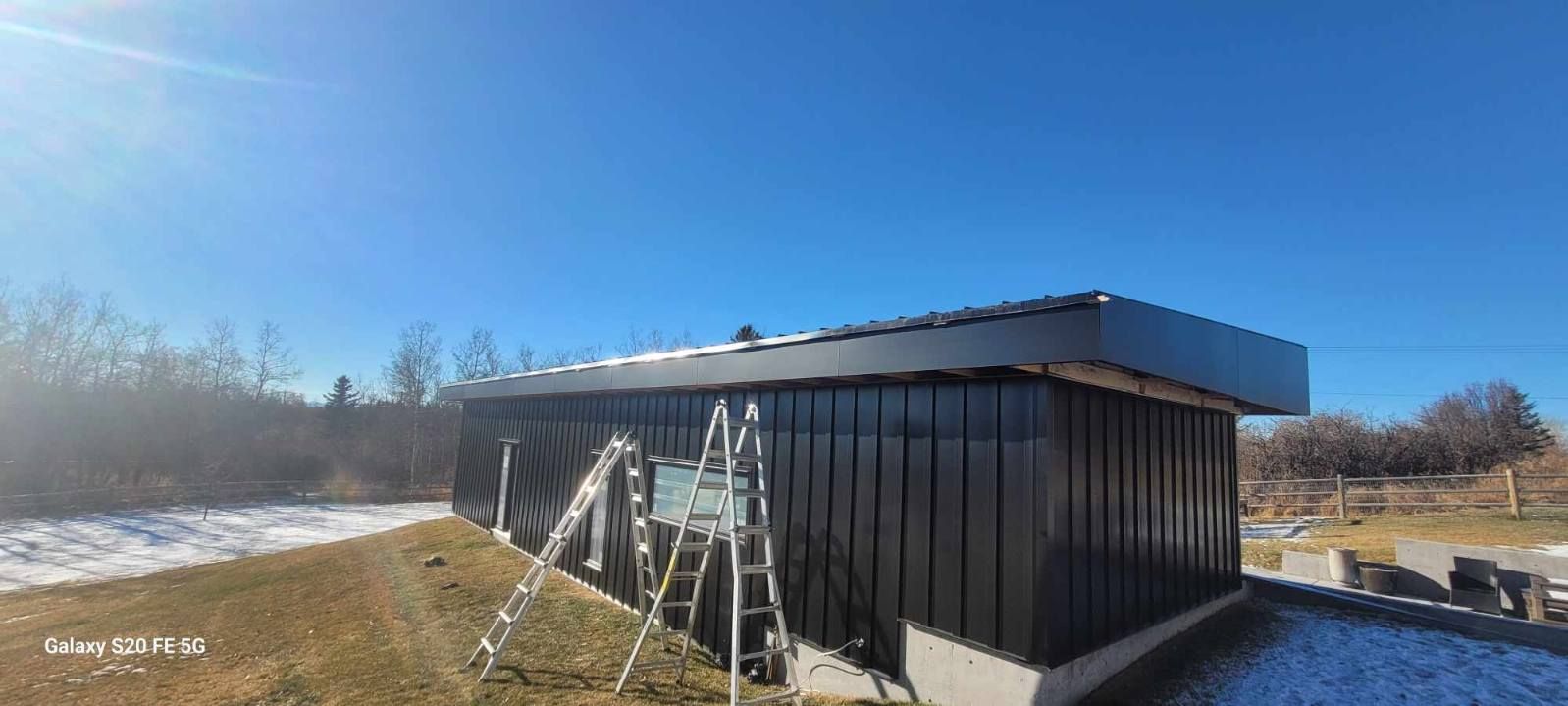 Black building with sloped roof beside a frosty field under a clear blue sky