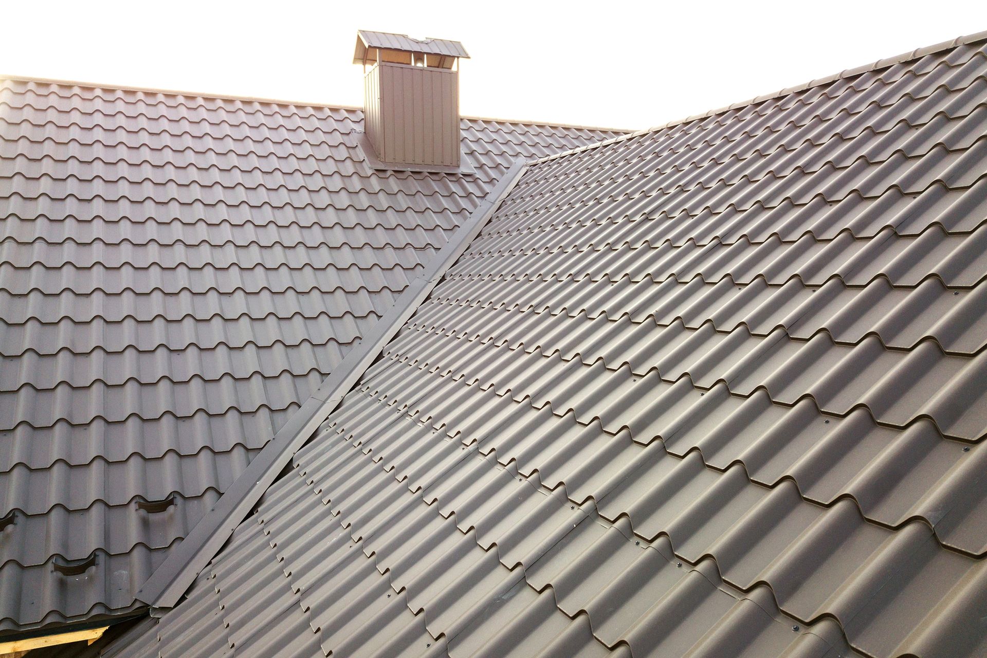 Sloped gray tiled roof with a chimney under a clear sky