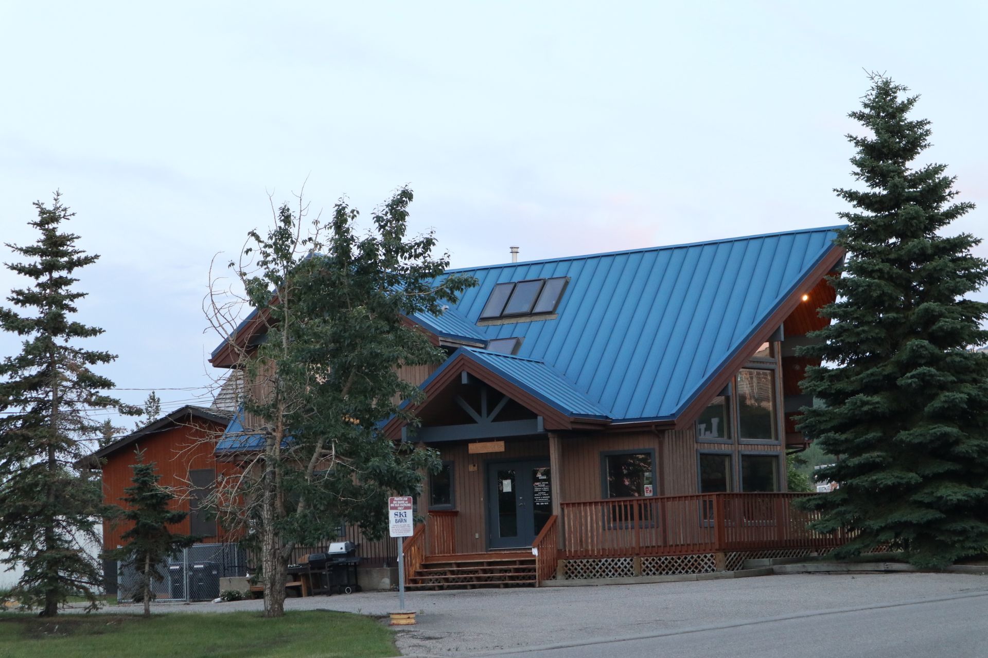 Rustic cabin with a blue metal roof and wooden porch, surrounded by trees at dusk
