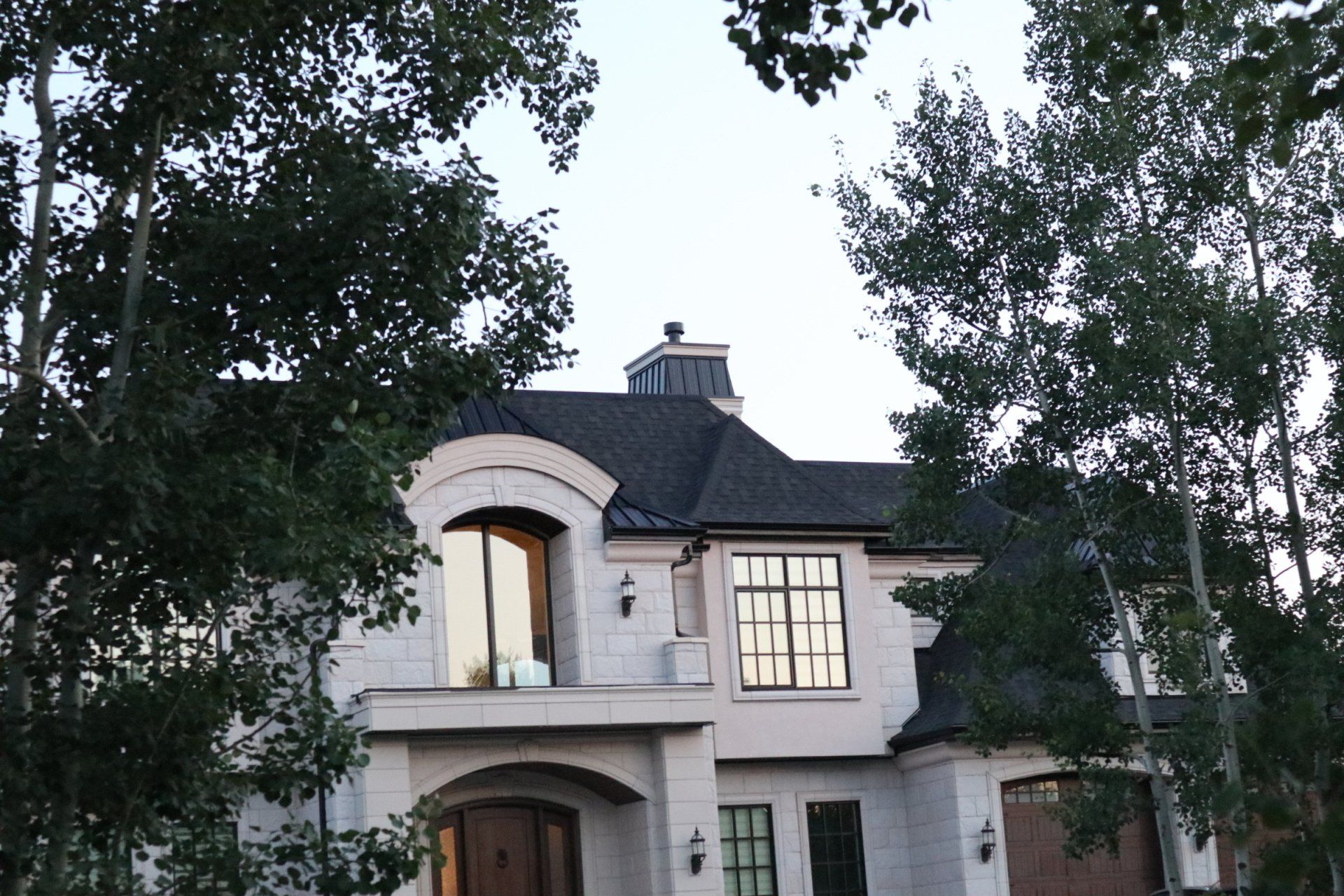 A large white house with a black roof is surrounded by trees