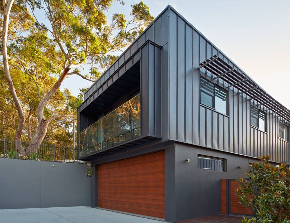 Modern black two-story house with wood garage door, large windows, and trees in the background