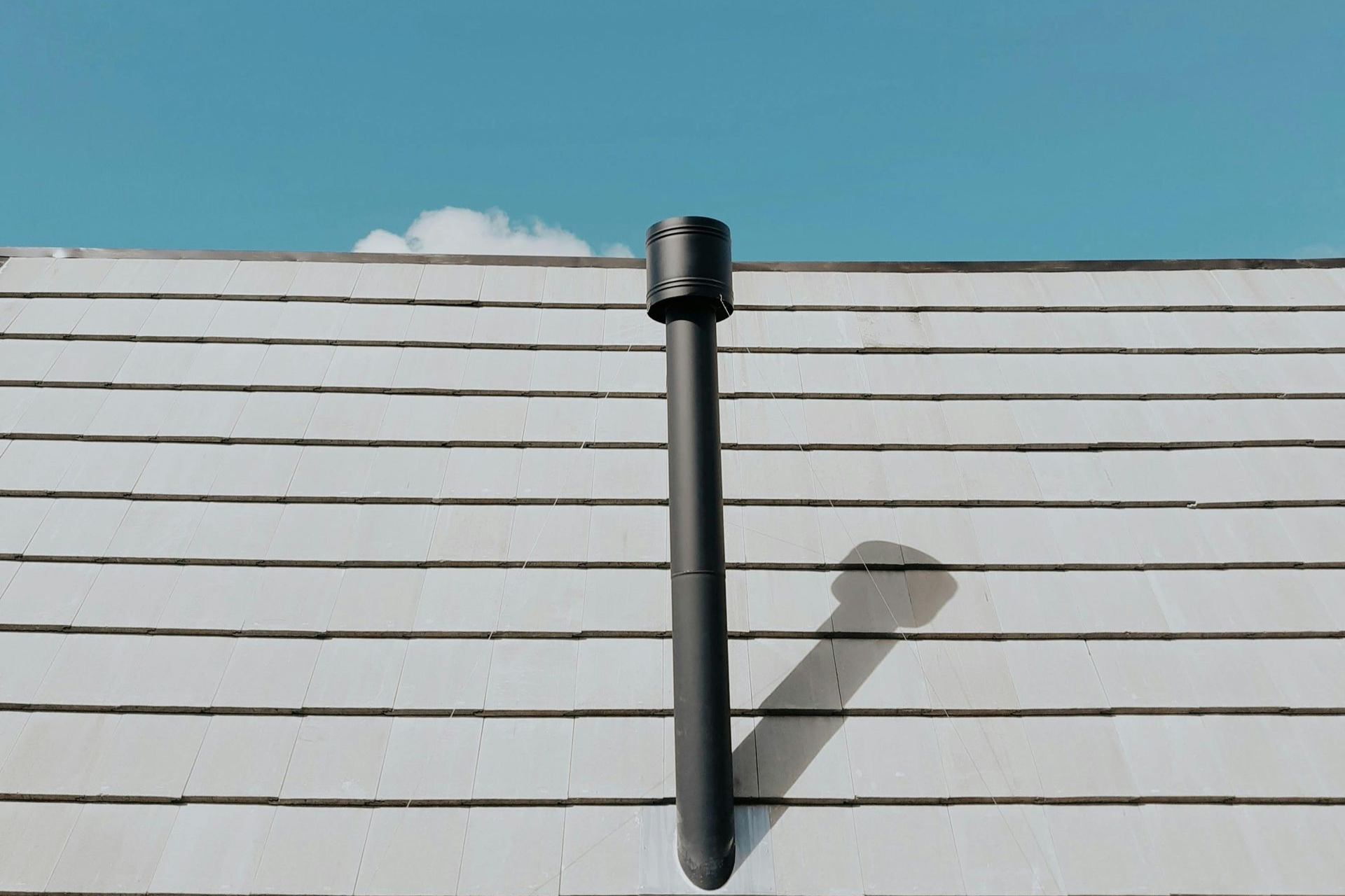 Black chimney pipe on a white rooftop against a blue sky with a few clouds.