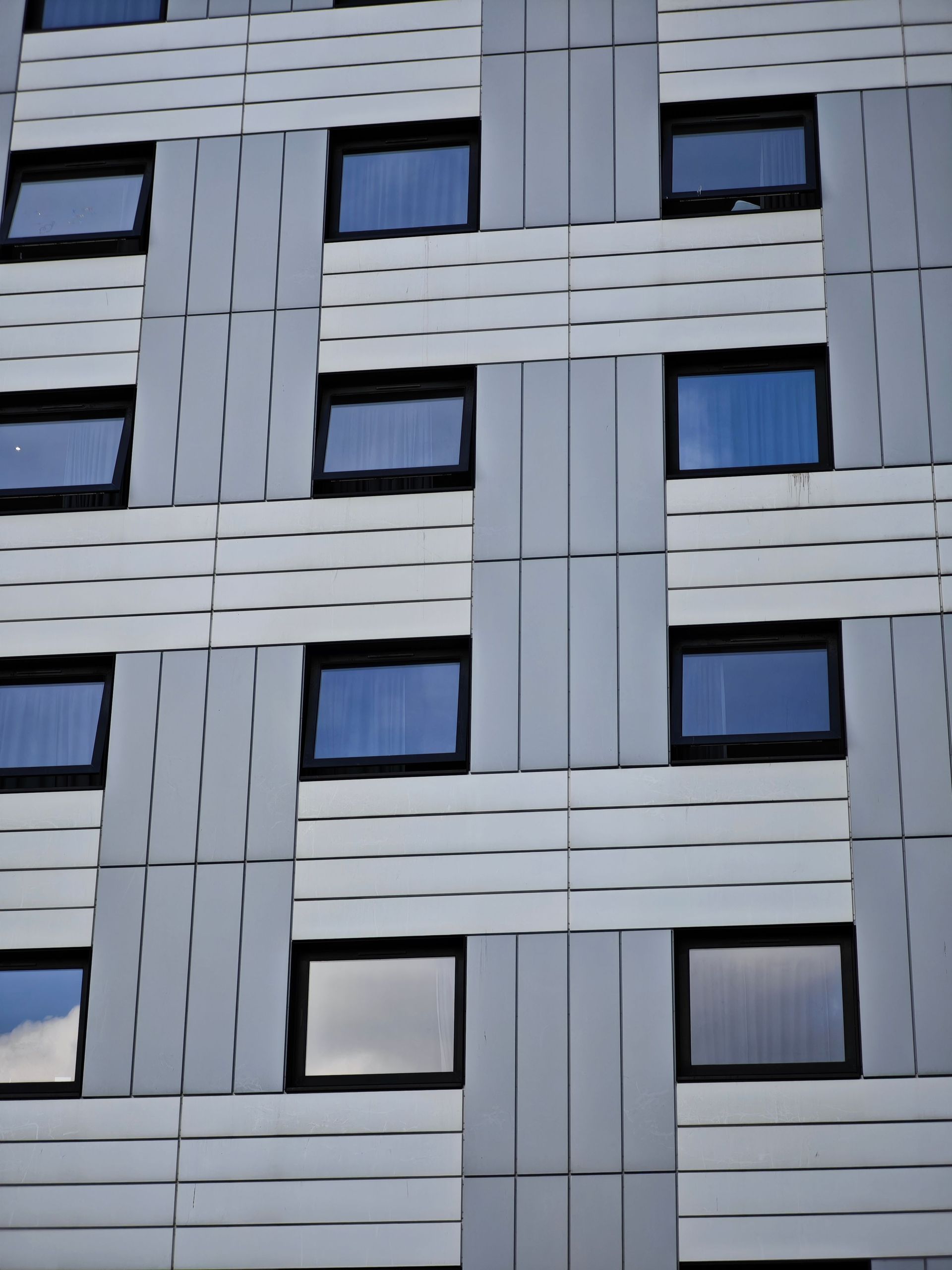 Close-up of a modern building facade with blue windows and gray paneling in a grid pattern