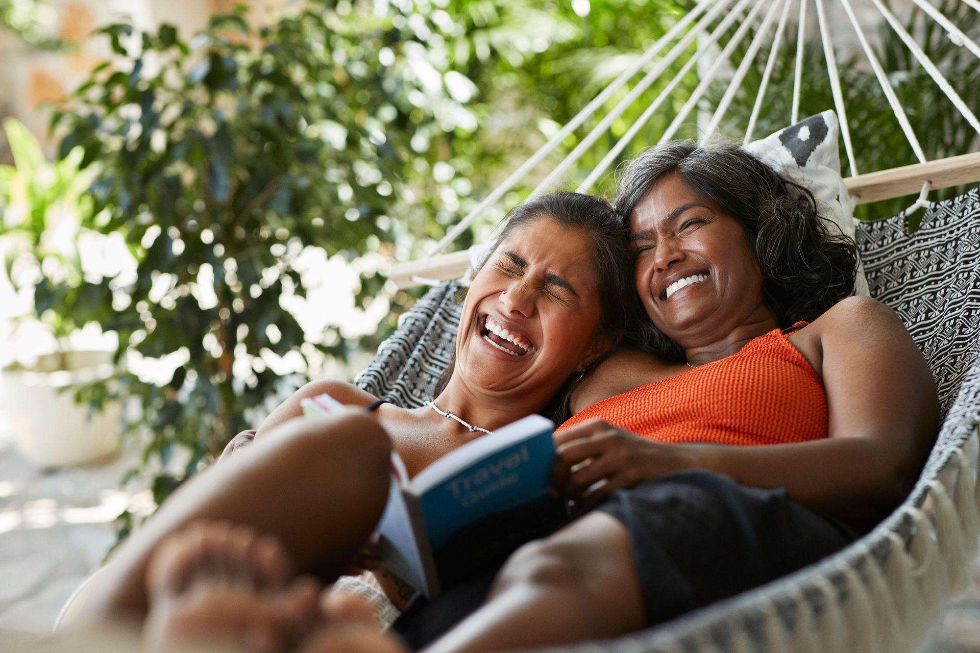 Two people relaxing in a hammock, smiling and reading a book outdoors.