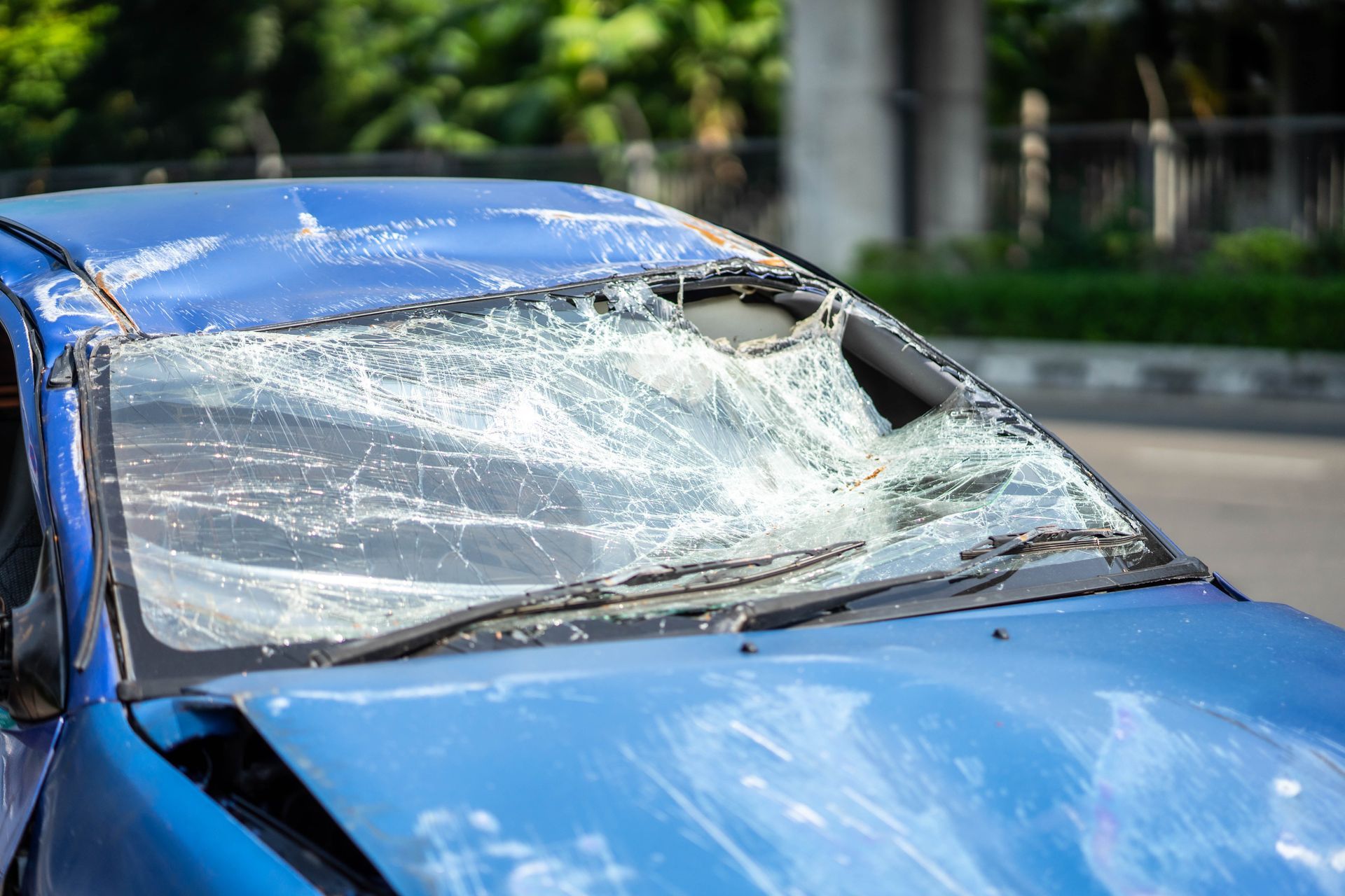 Damaged blue car with shattered windshield on a road.