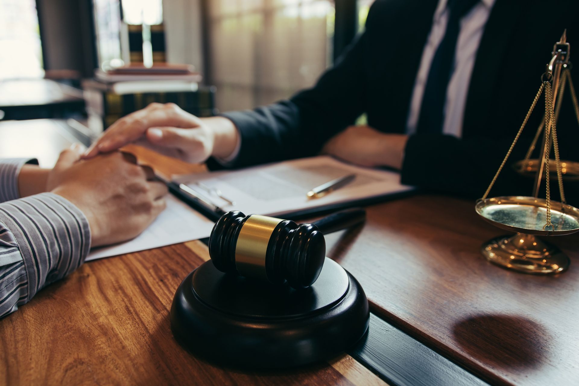 Lawyer comforting a client, gavel, scales of justice, documents on a wooden table.