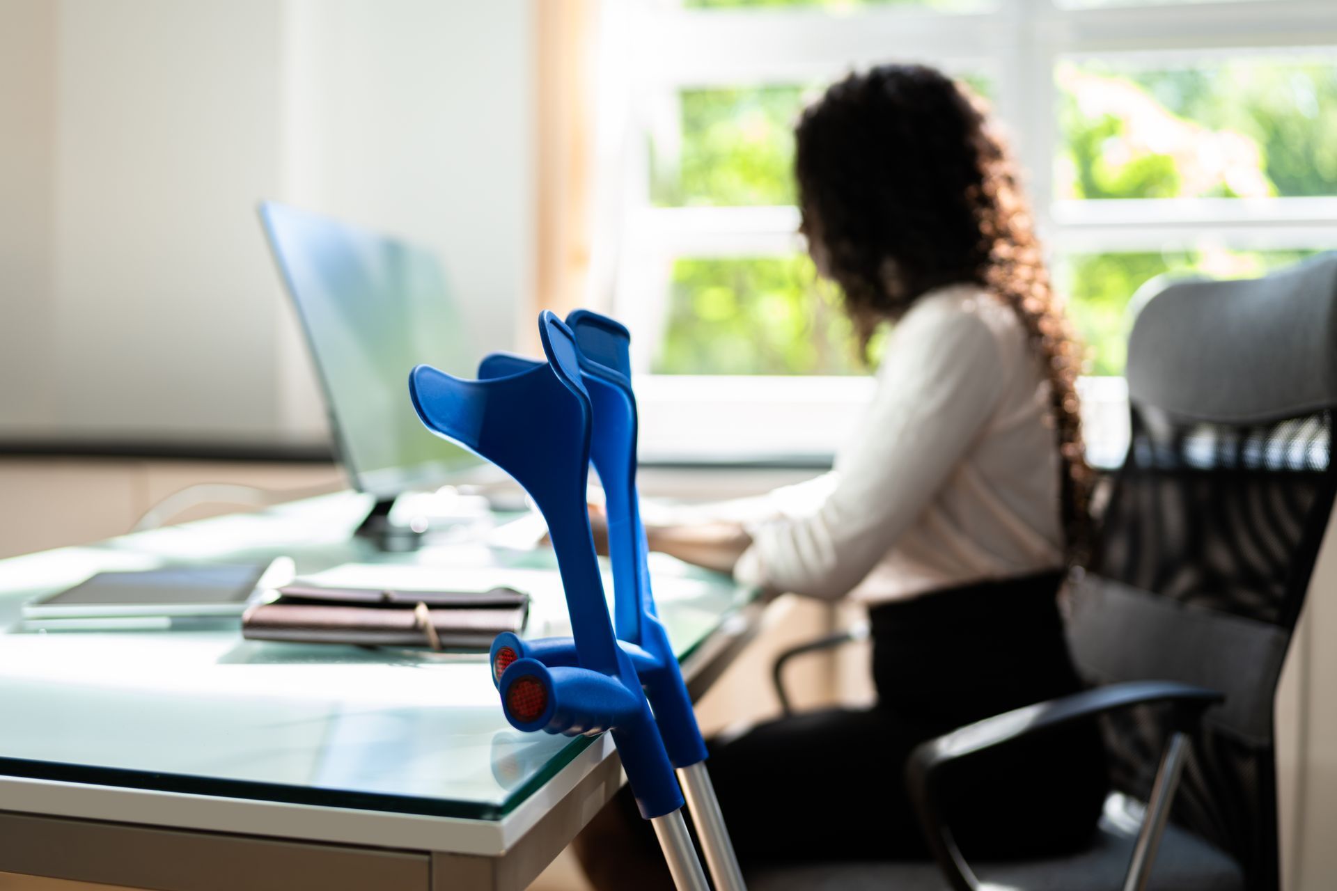 Blue crutches on desk in front of person using computer in office setting.