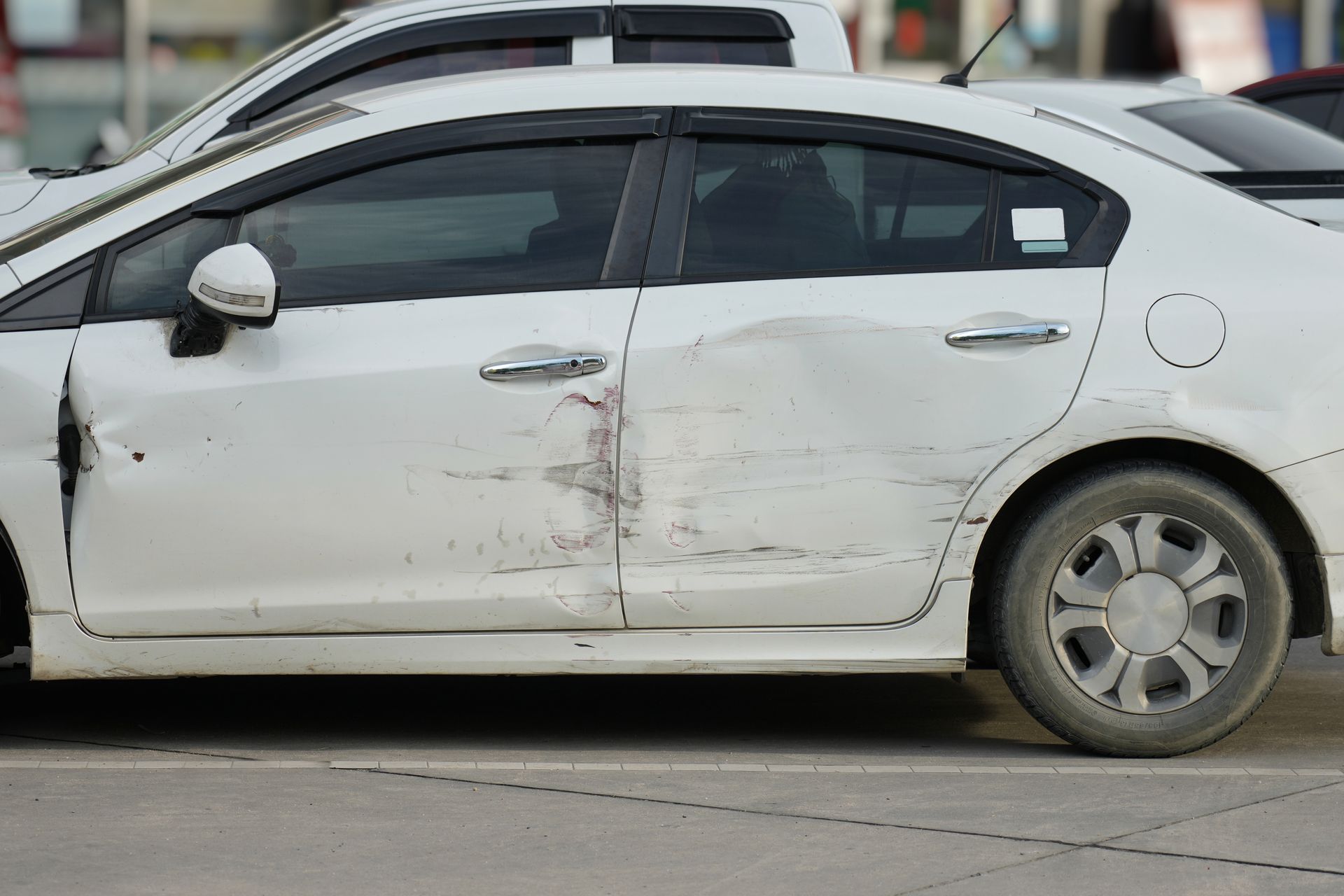 White car with significant damage to the driver's side doors.