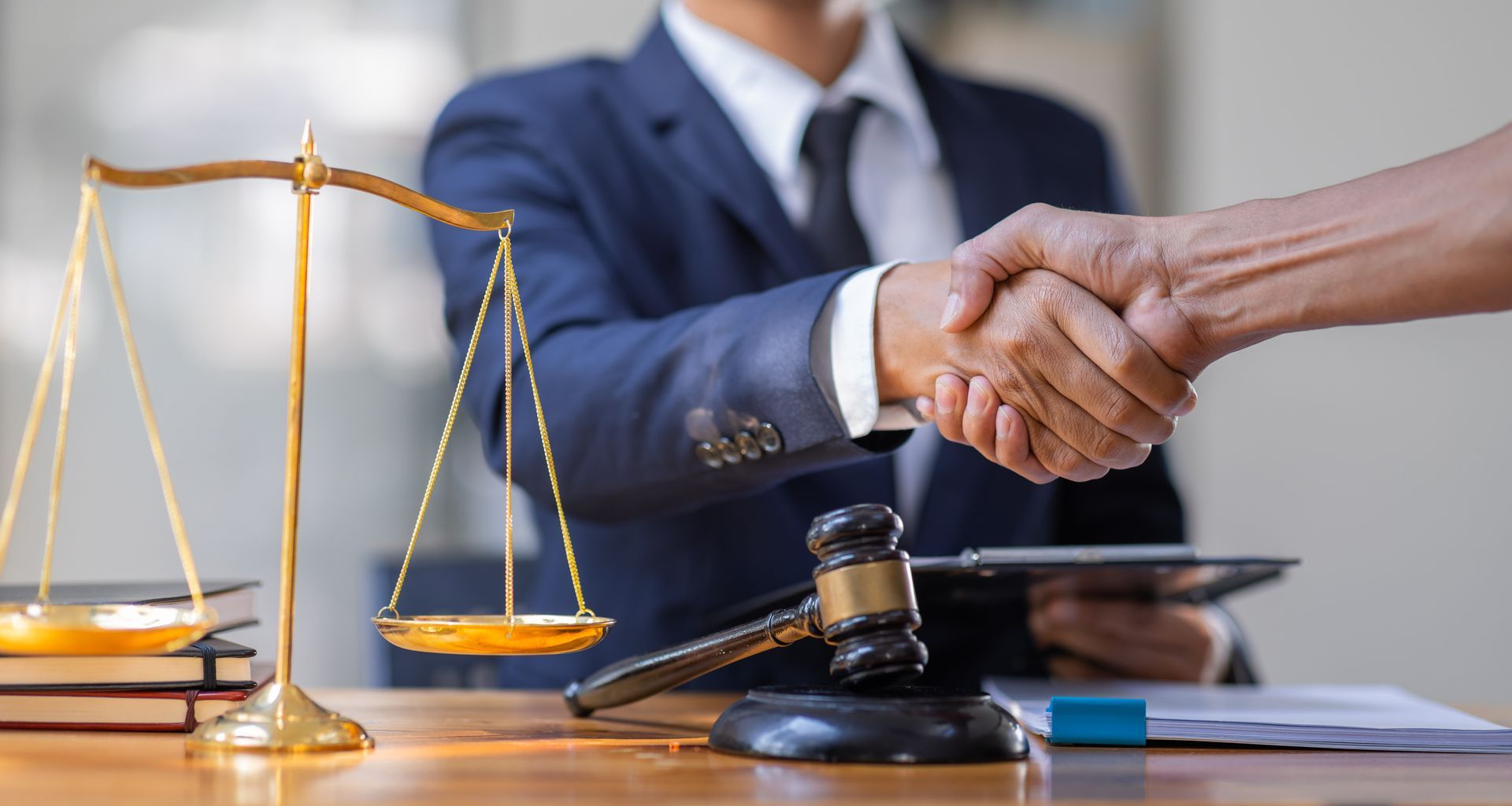 Lawyer shaking hands with a client, with scales of justice and gavel on the desk.