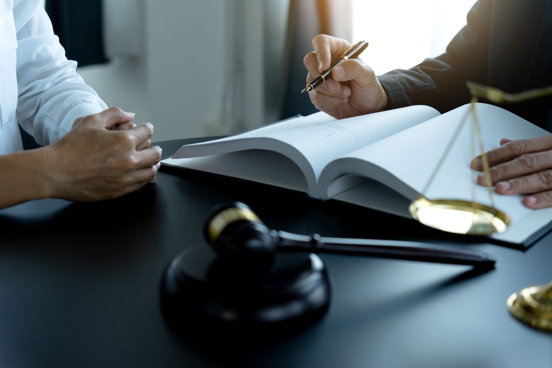 Legal consultation with open book, gavel, and scales on a desk.