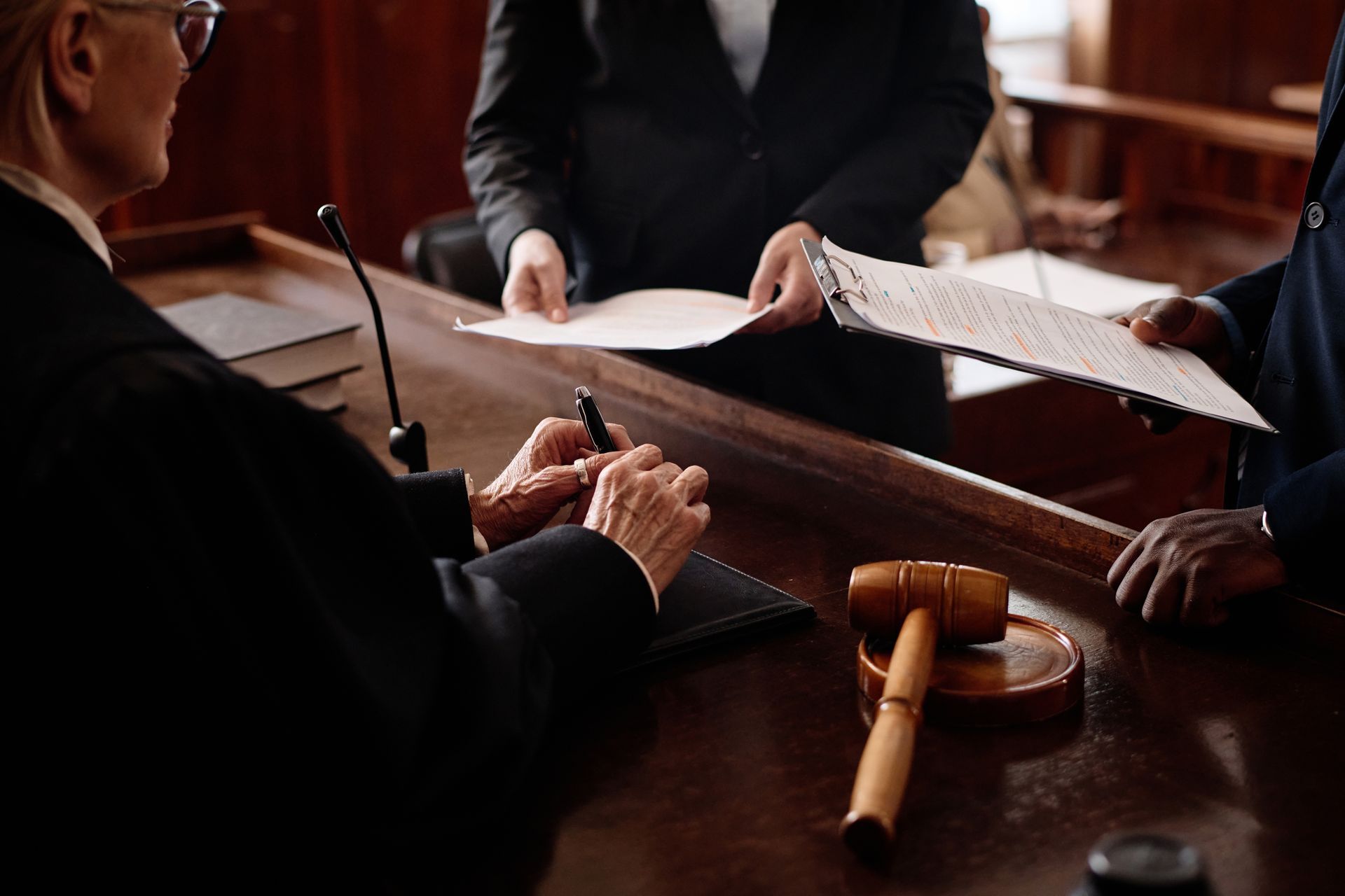 Judge signing documents in a courtroom with lawyers present and gavel on the desk.