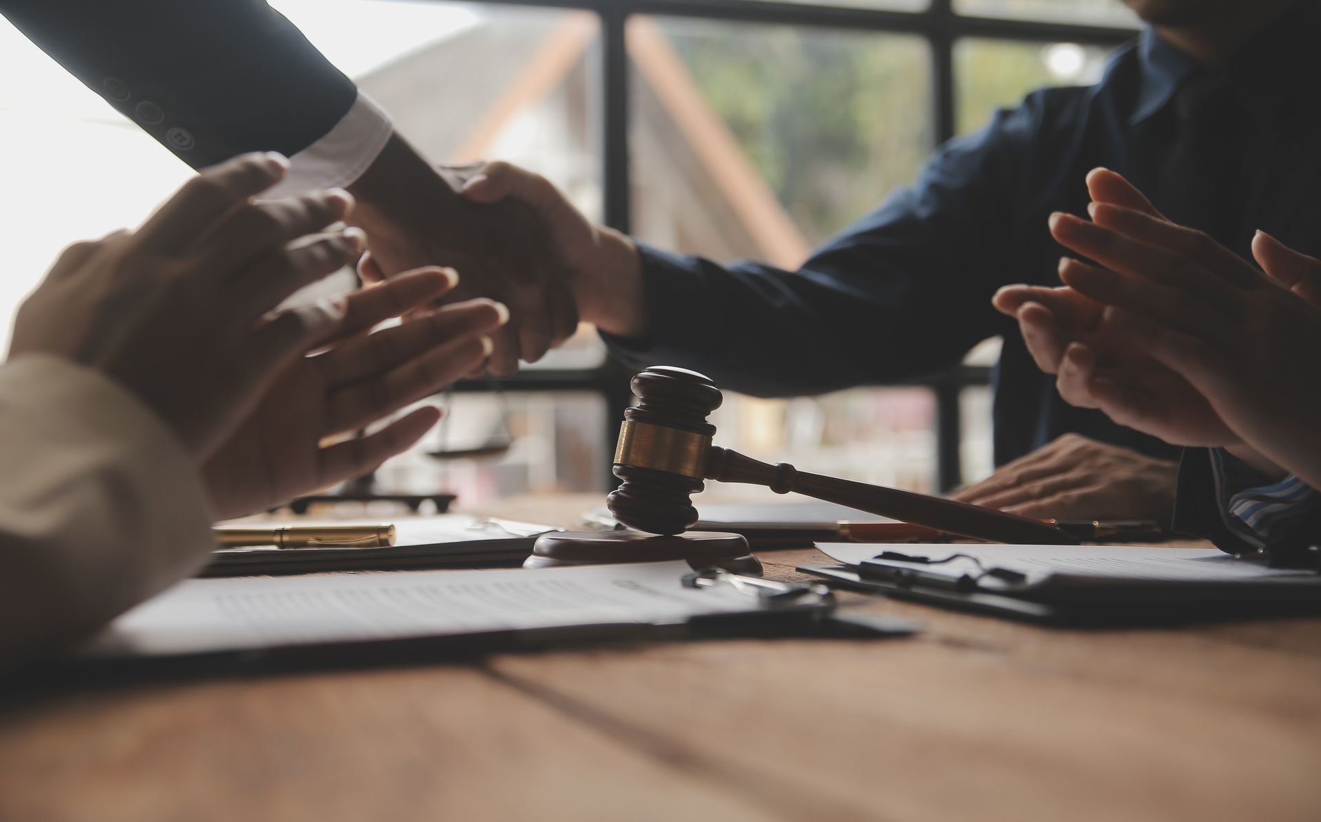 Two people shaking hands over a table with a gavel, others clapping.
