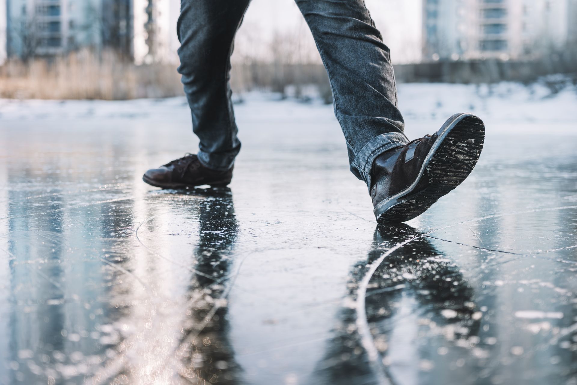 Person walking on a frozen lake; close-up of feet and legs in dark jeans and shoes on ice.