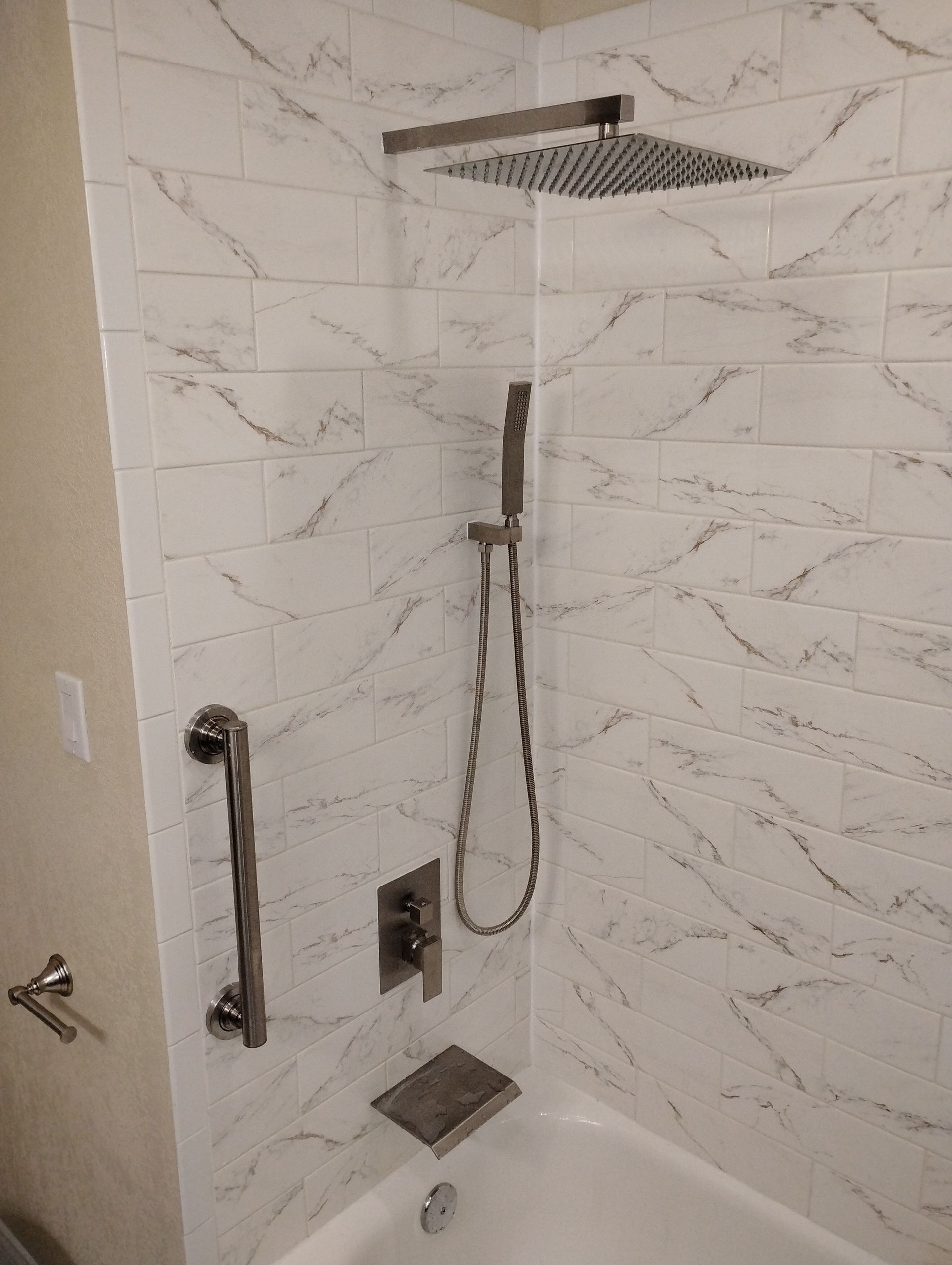 Accessible shower with grab bar, handheld showerhead, bench, and marble tile walls.