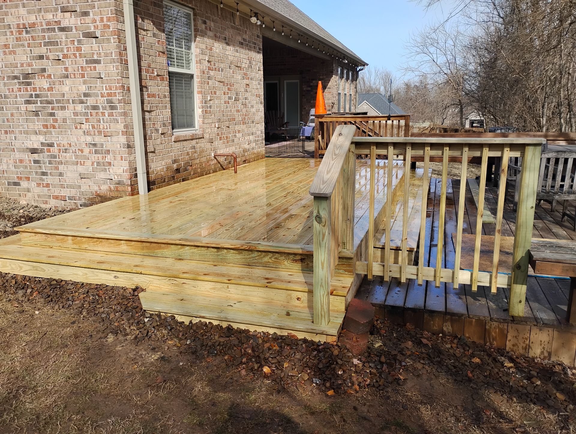 Back patio with wet wooden deck and railing beside a brick house under construction