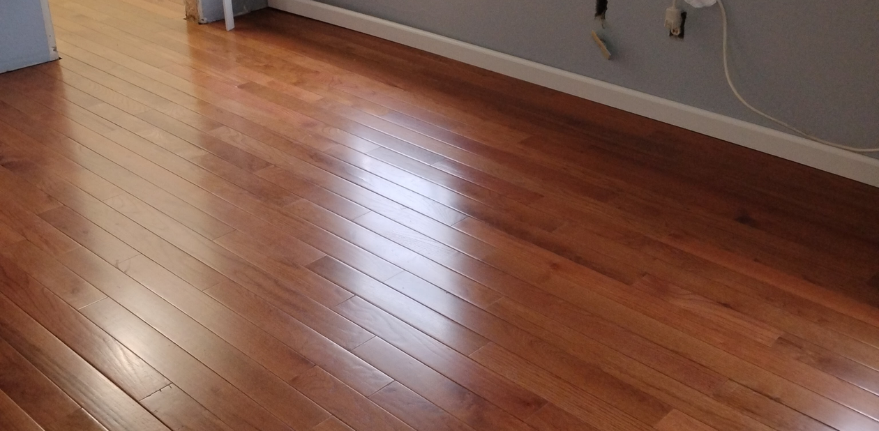 Wooden floorboards in a room with a baseboard and wall visible in the background