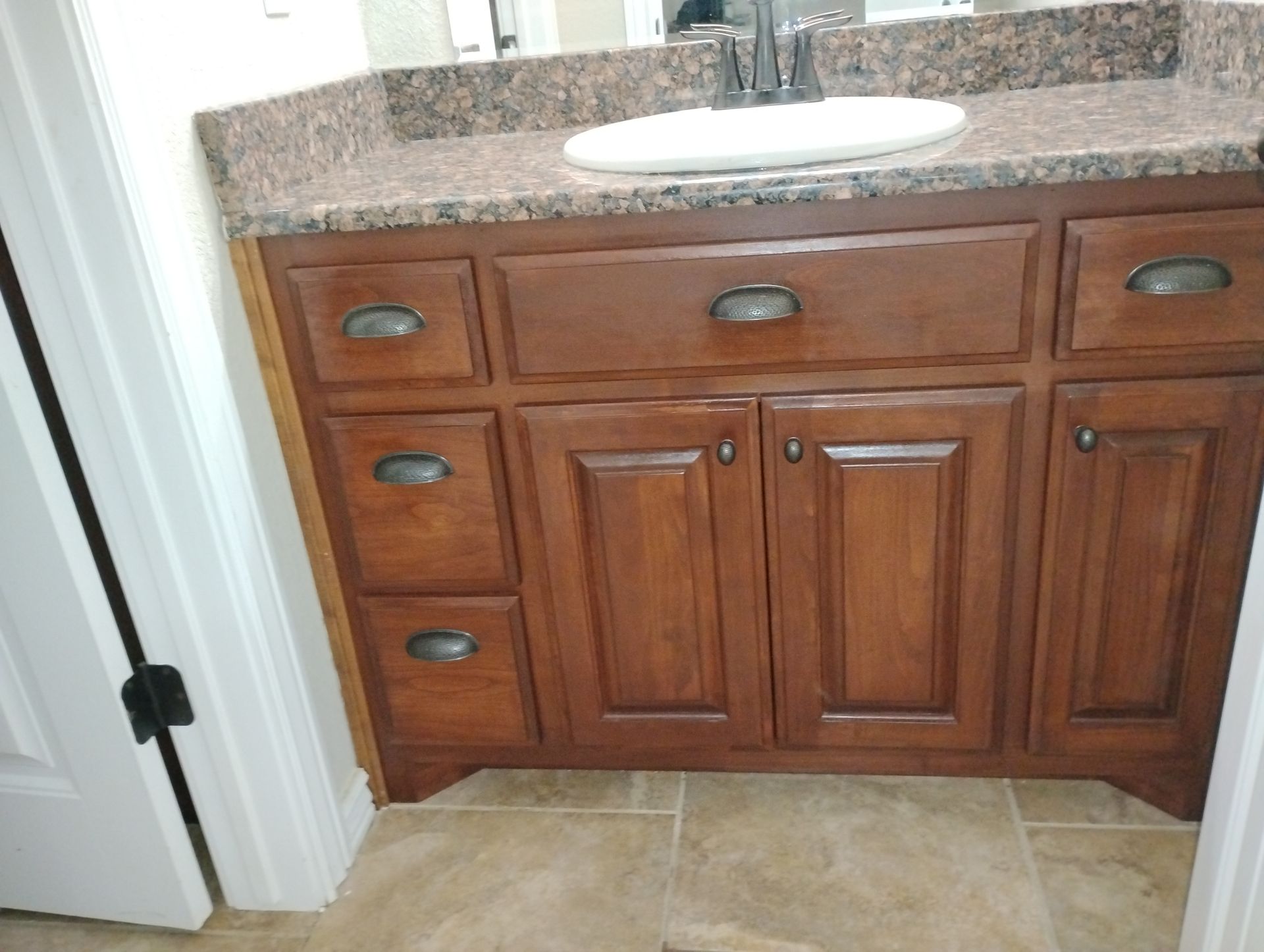 Bathroom vanity with brown cabinets, granite countertop, and white sink beneath a mirror