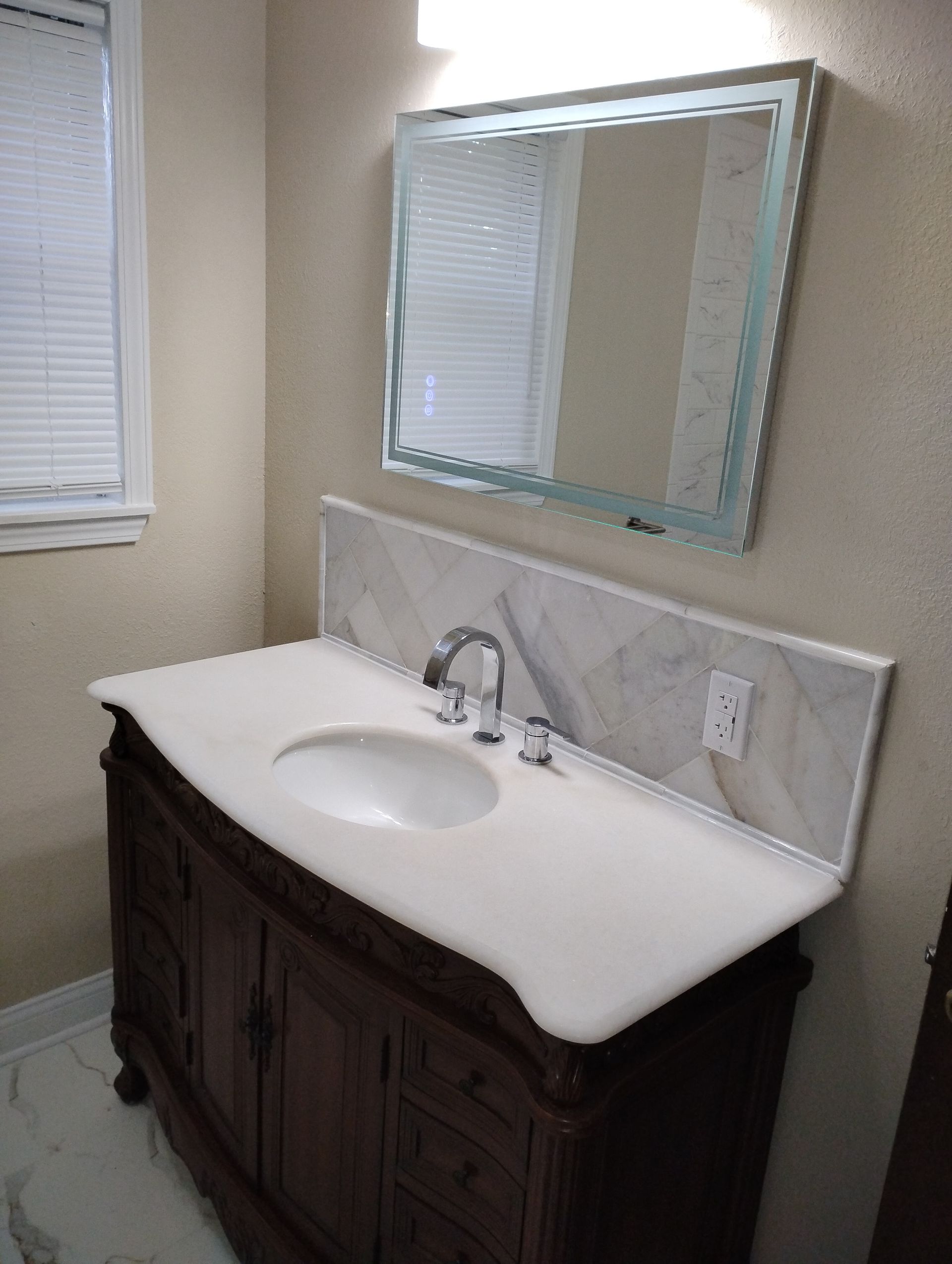 Bathroom vanity with white sink, dark wood cabinet, and framed mirror on beige wall.