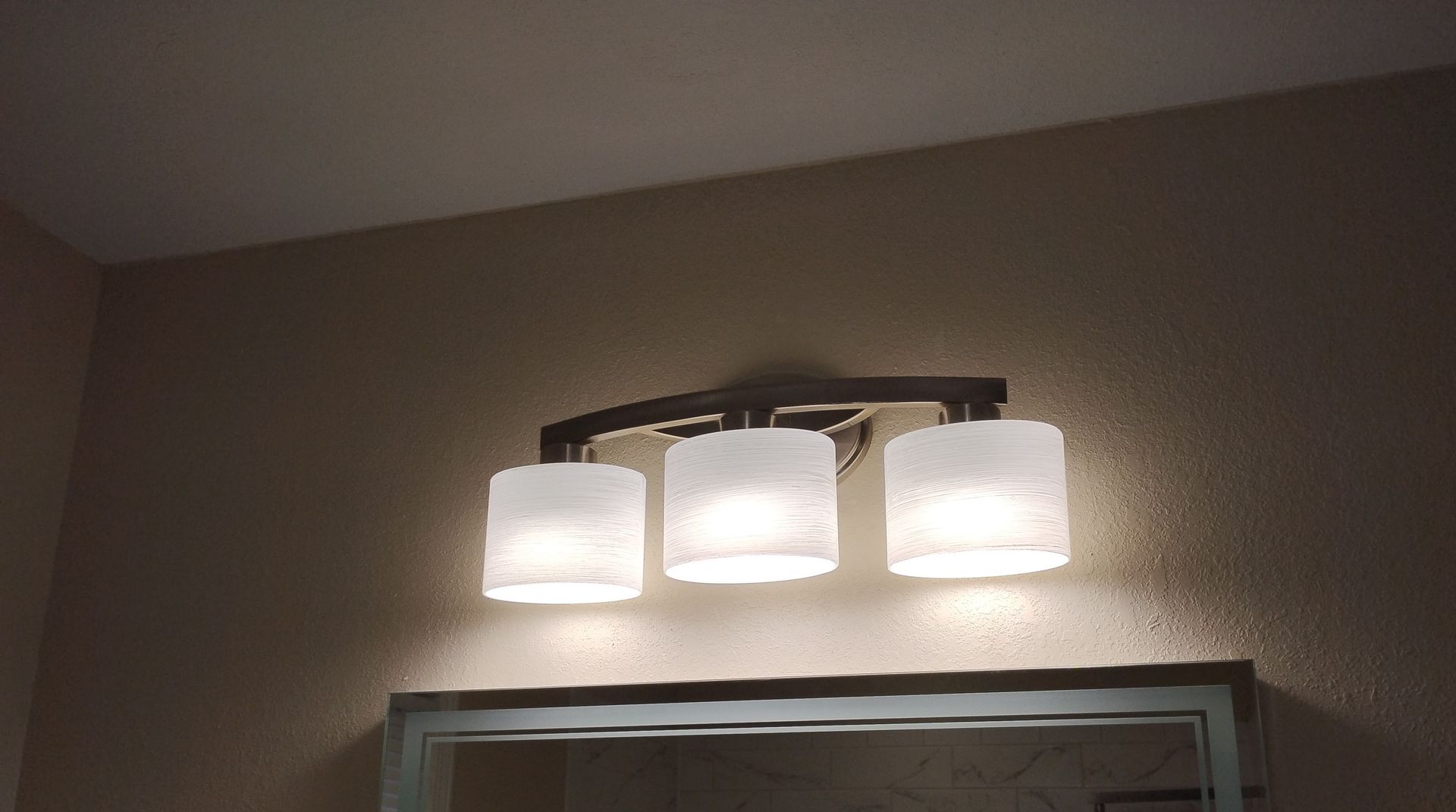 Three-light bathroom vanity fixture with frosted glass shades mounted above a mirror
