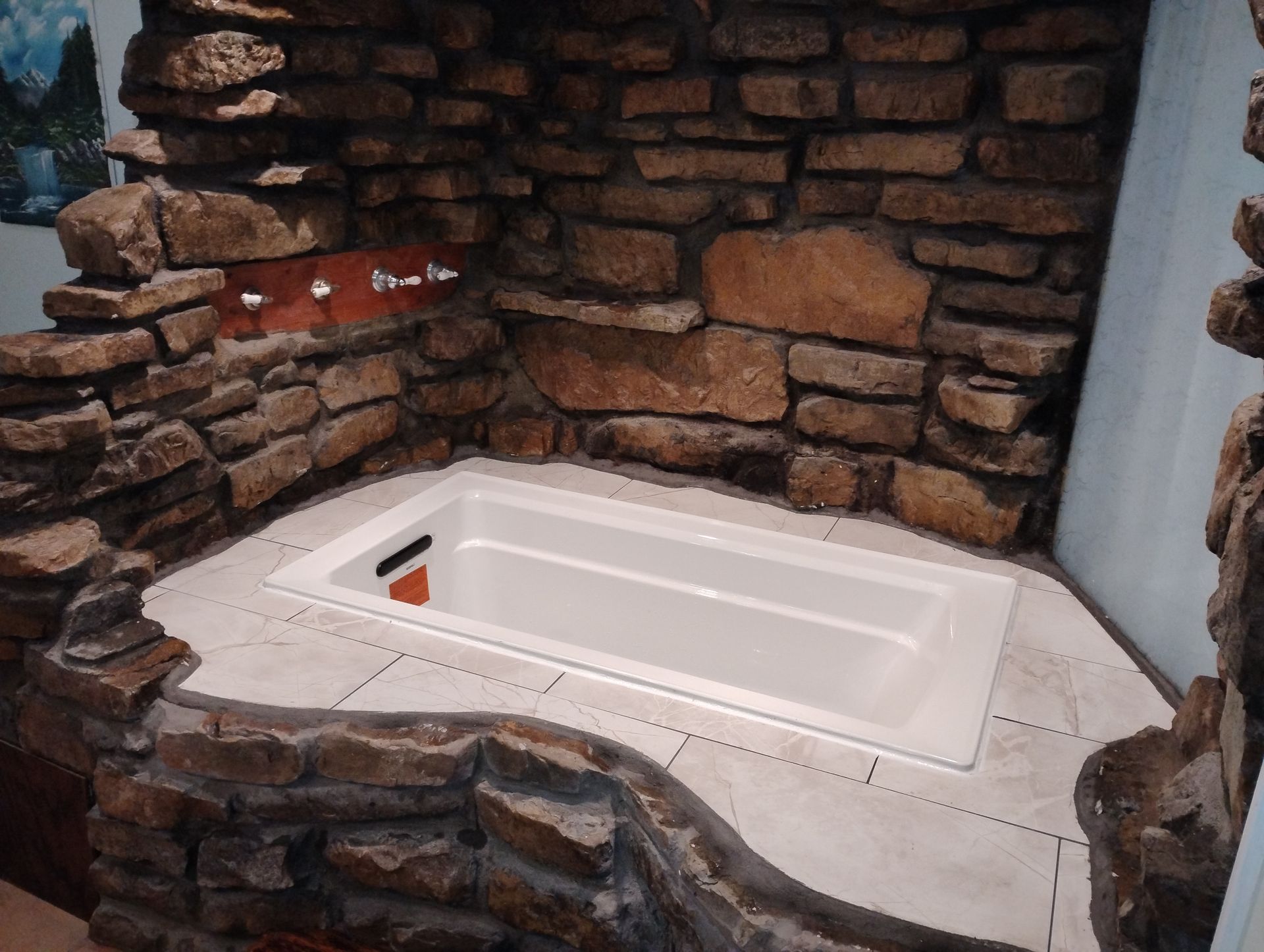 Small white bathtub set into a rustic stone alcove with tiled floor.