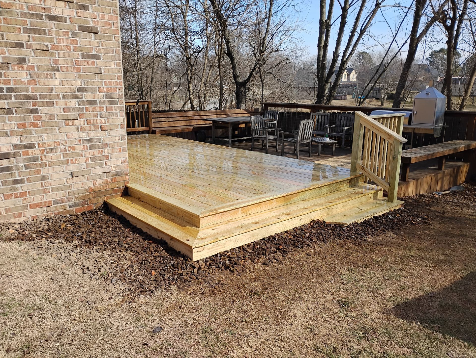Wooden backyard deck with steps beside a brick house, surrounded by mulch and bare trees