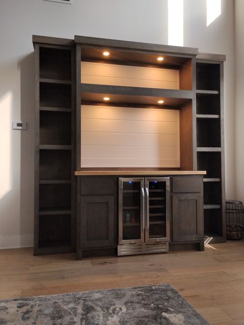 Modern built-in dark wood entertainment cabinet with shelves, lights, and a glass-front mini fridge