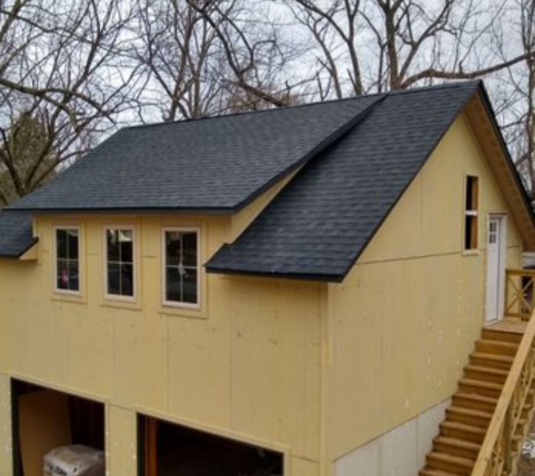 Yellow house with dark gray roof and exterior stairs on a wooded hillside