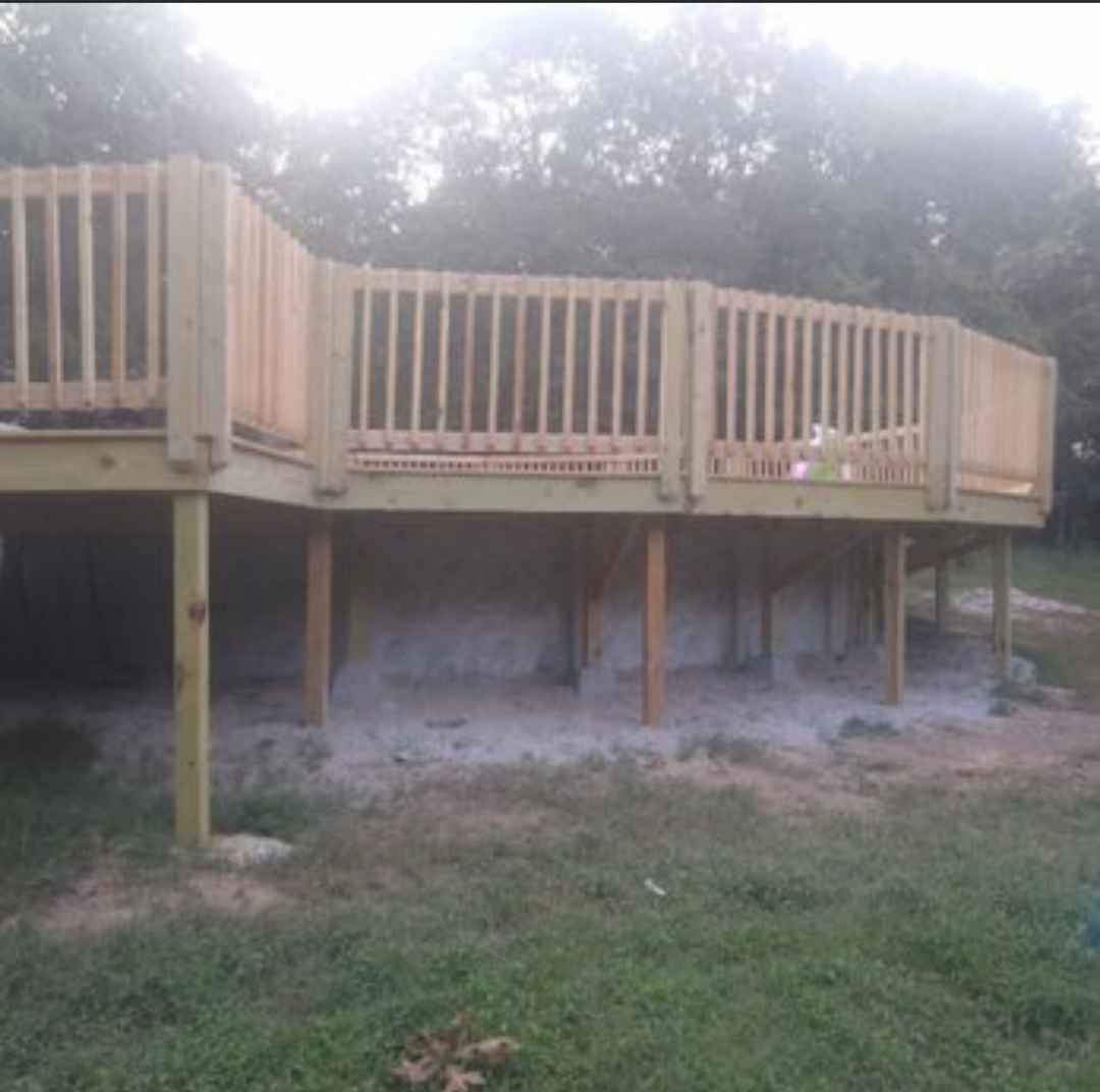 Wooden raised deck with railing and stairs, set on posts over a grassy yard at dusk.