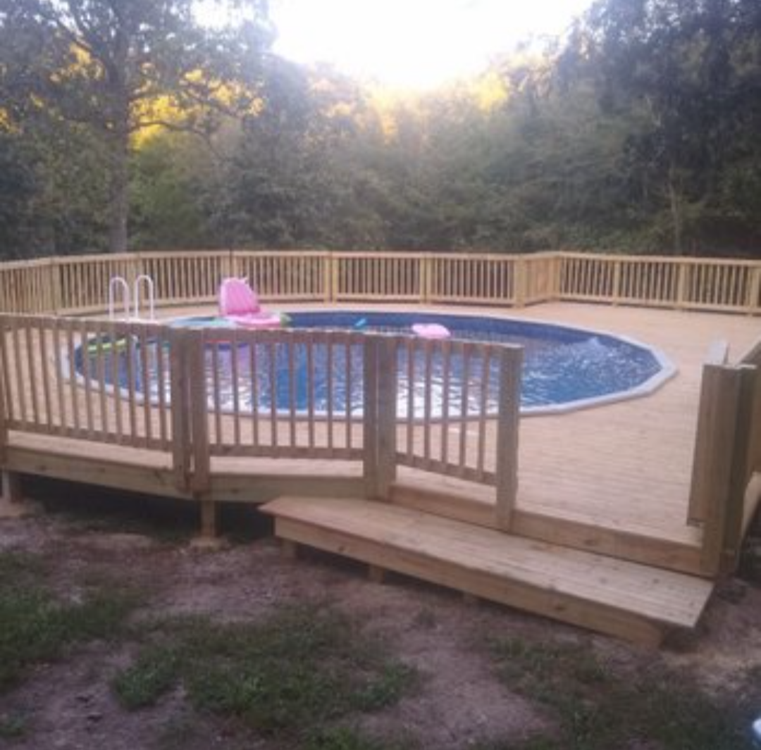Above-ground pool with wooden deck and railing in a wooded backyard at sunset