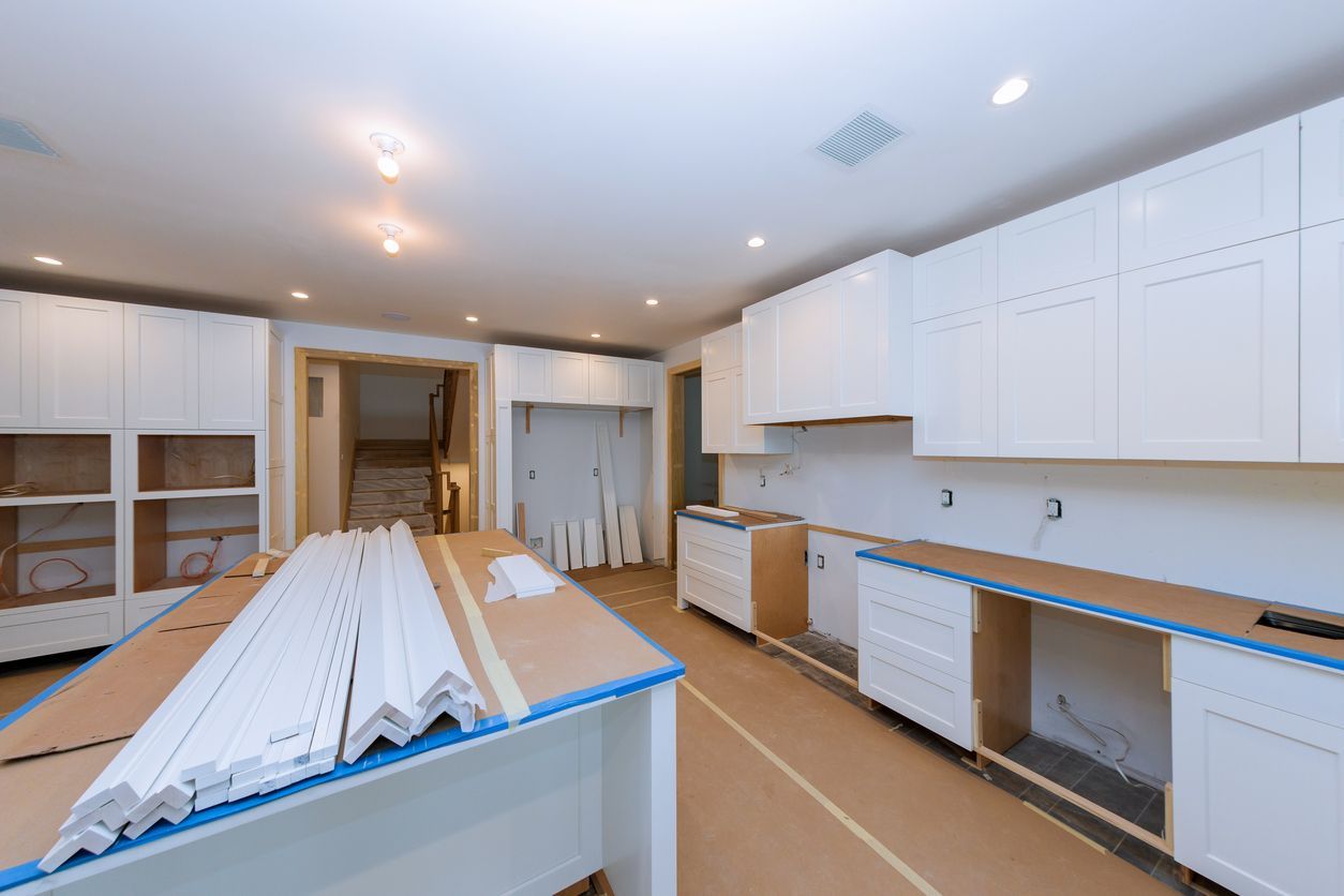 Unfinished white kitchen with cabinets, countertops, and construction materials on the floor and island.