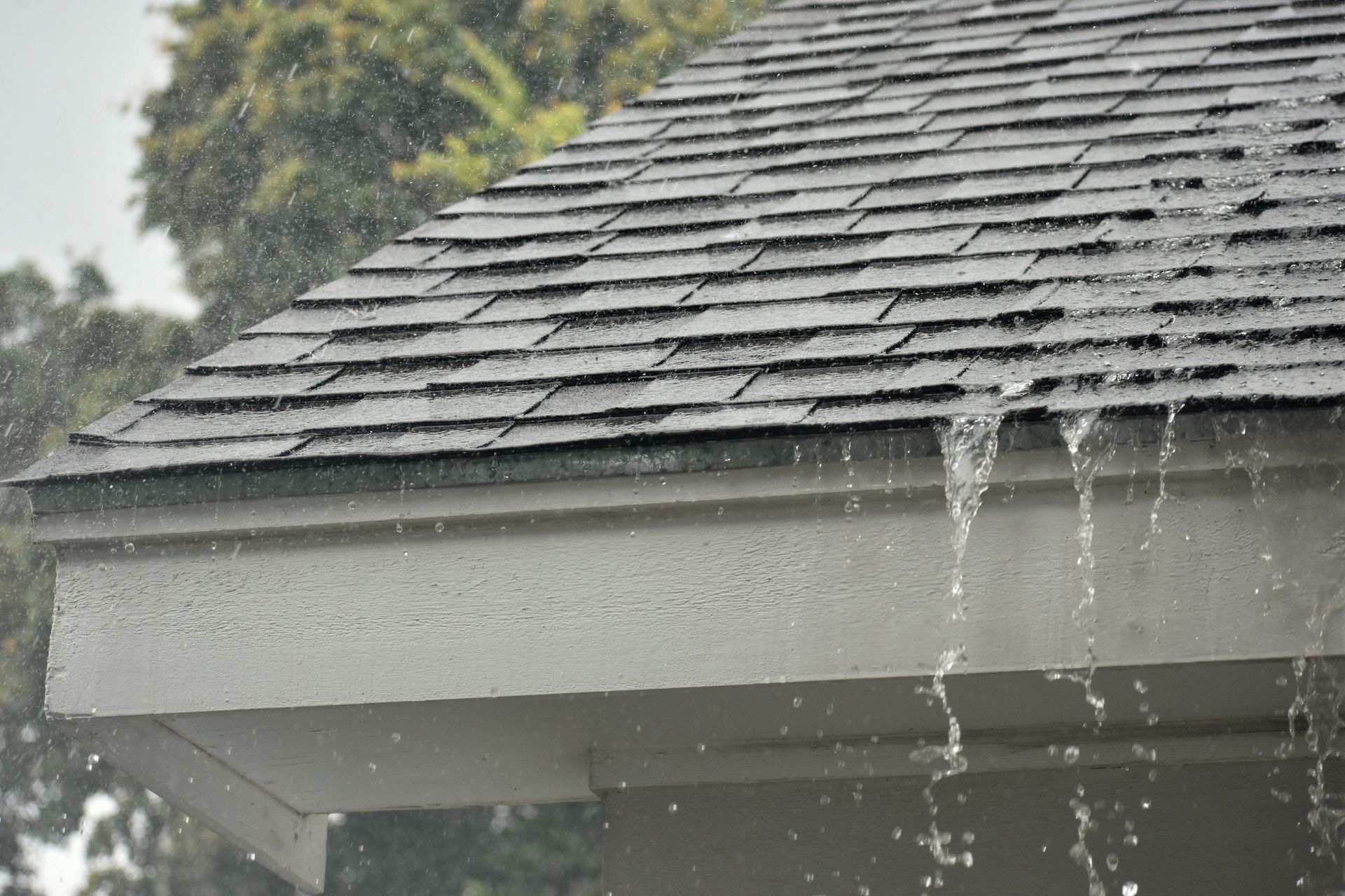 Rainwater streaming off a gray shingled roof eave during a storm