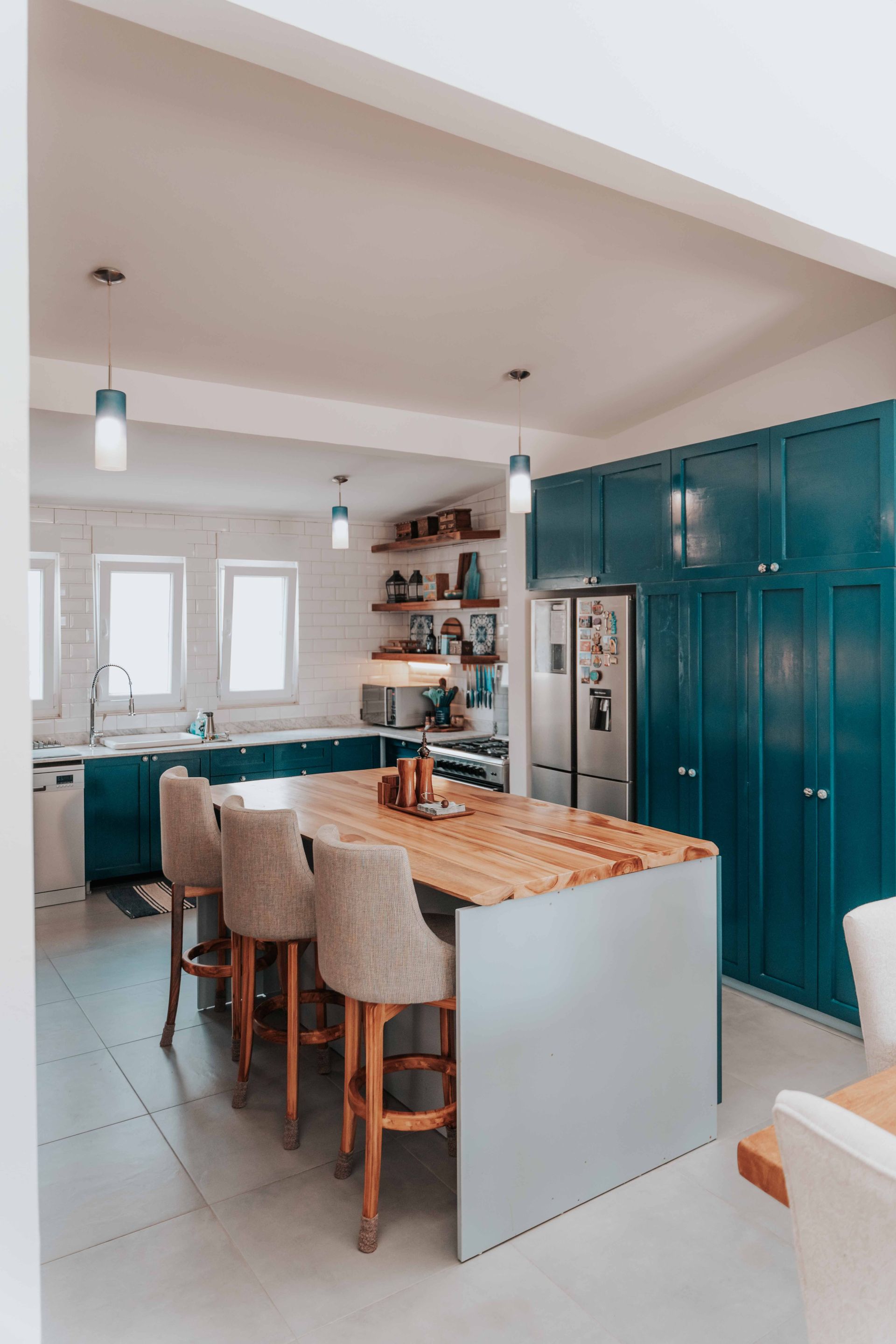 Modern kitchen with teal cabinets, island, bar stools, and stainless steel appliances
