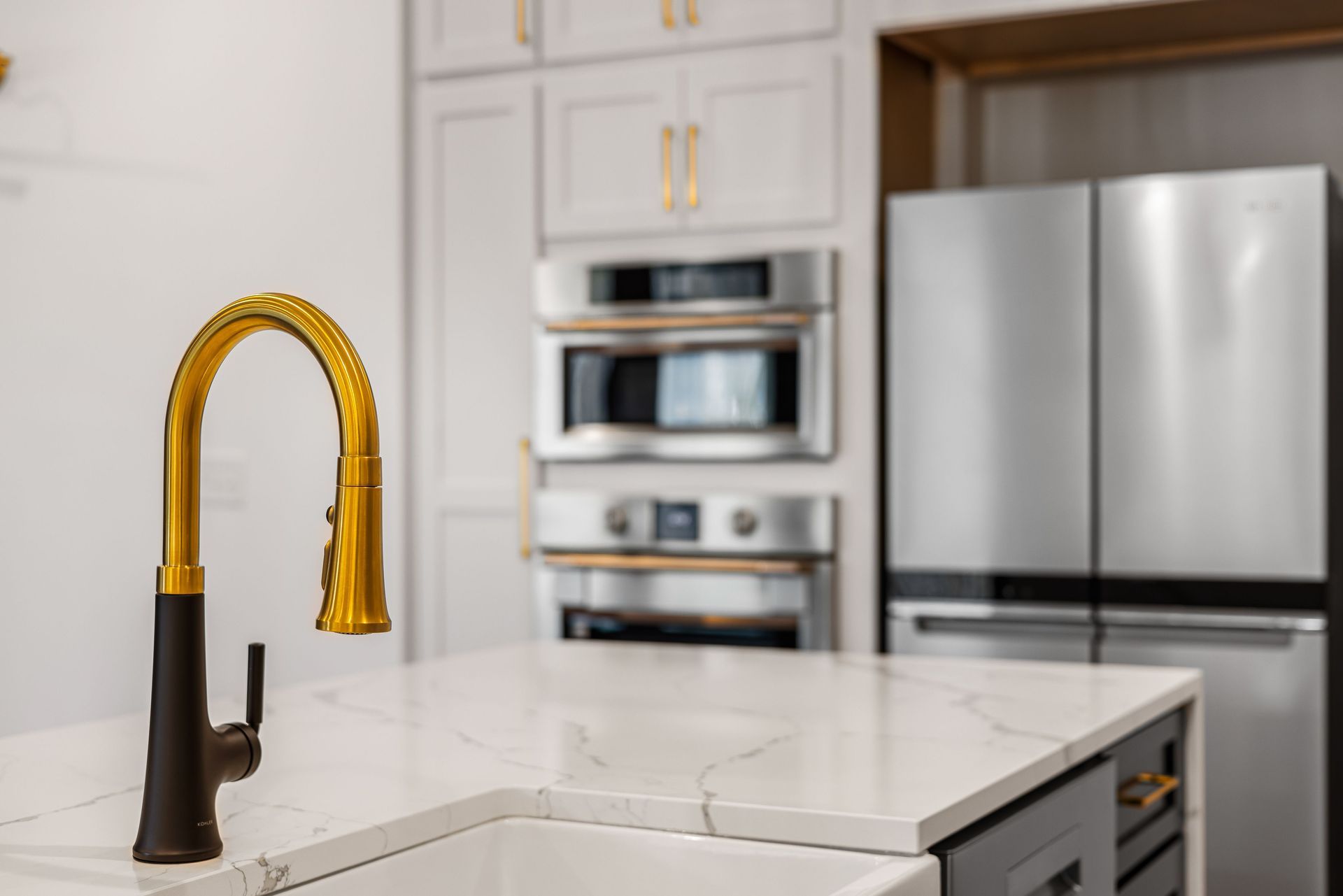 Modern kitchen with gold faucet, white island, and stainless steel appliances