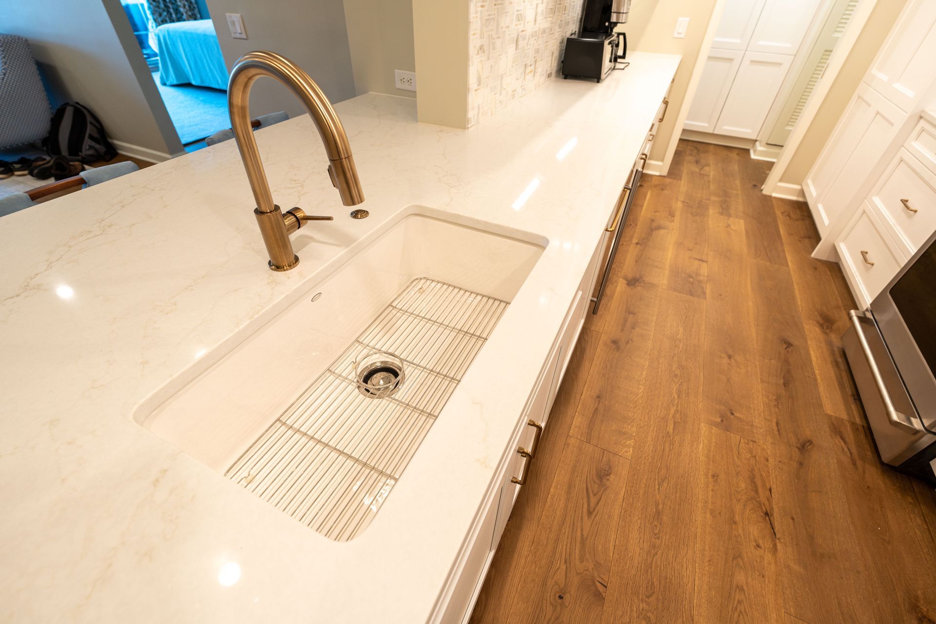 Modern kitchen with white countertop, farmhouse sink, brass faucet, and wood floor corridor