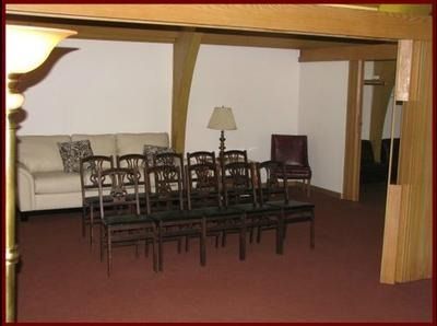 Empty meeting room with stacked chairs, a couch, a lamp, and burgundy carpet