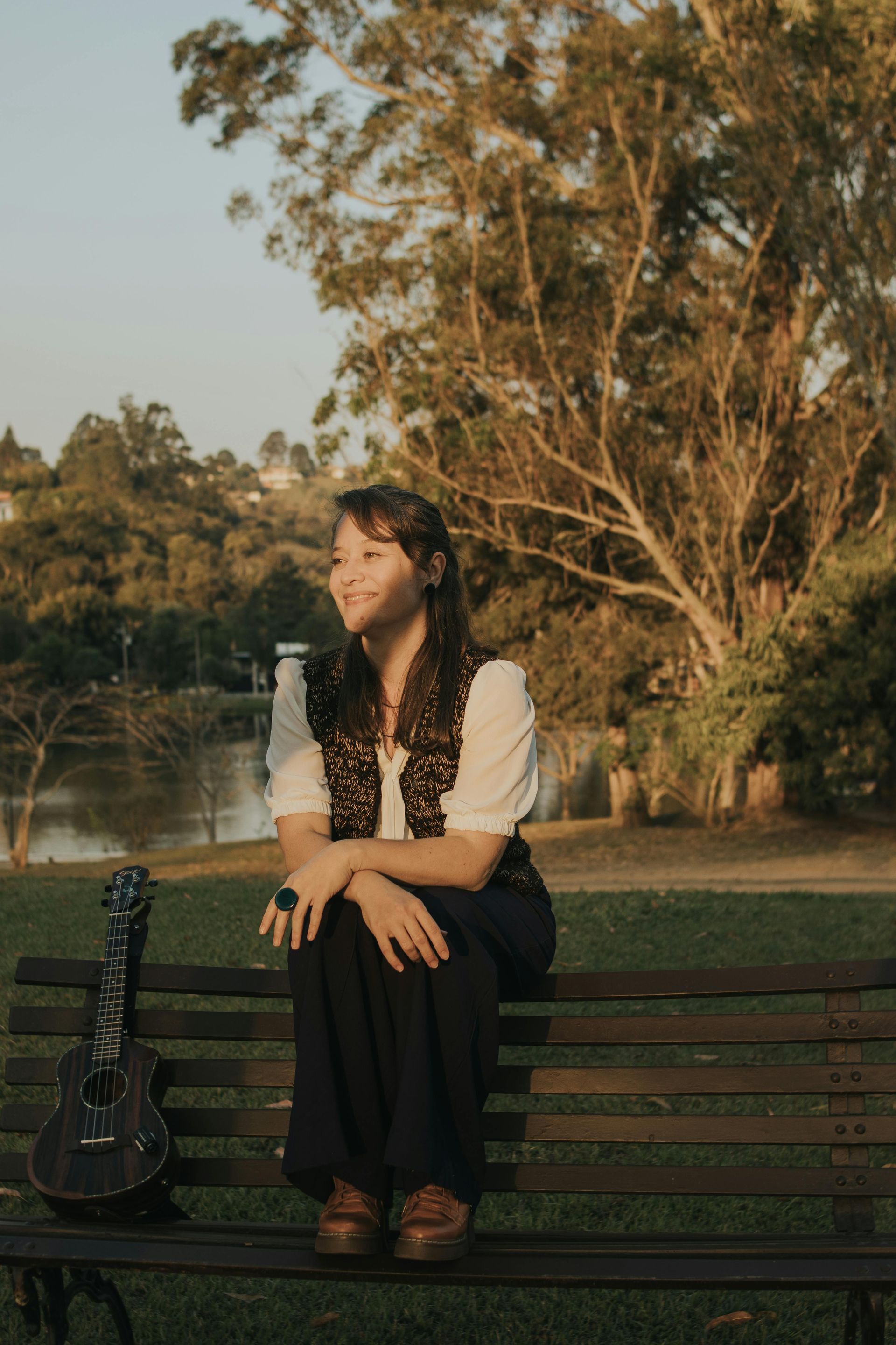 Woman sitting on a park bench beside a bottle, with trees and grass in warm evening light