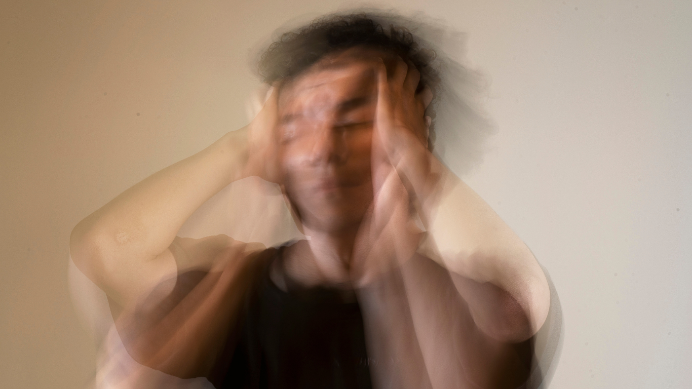 Blurred person with hands on head, appearing distressed against a plain background