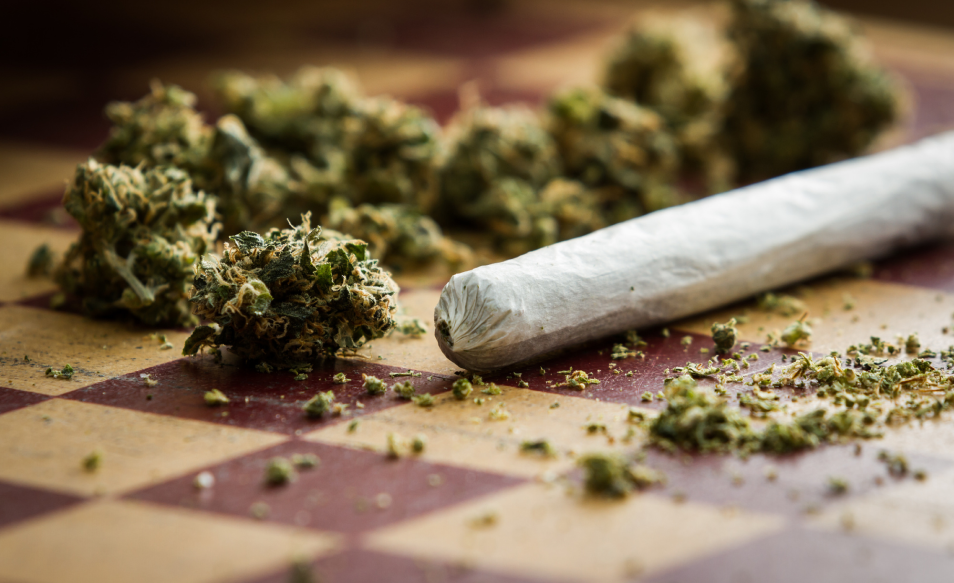 Loose cannabis buds beside a rolled joint on a chessboard-patterned surface