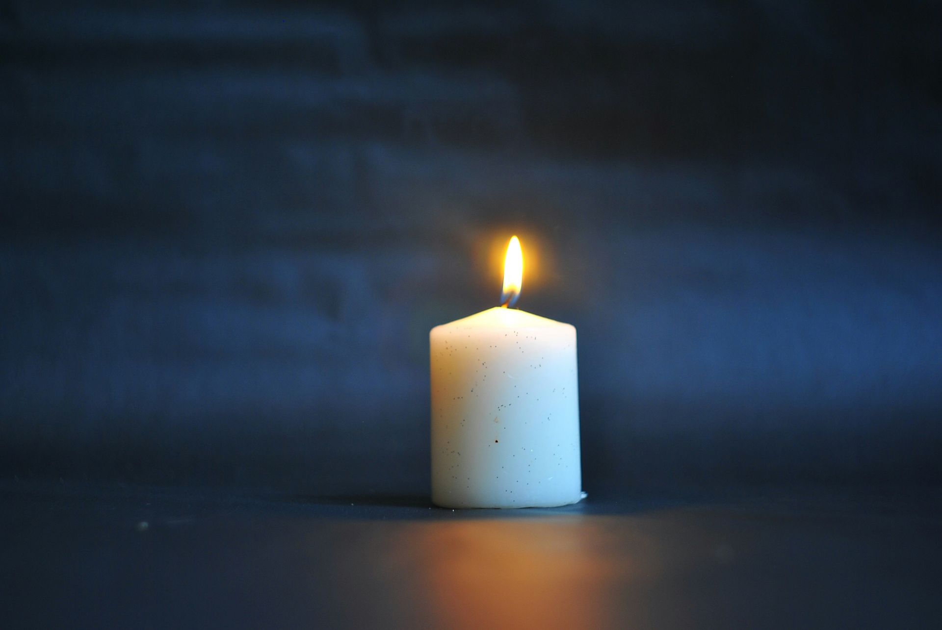 Single lit white candle on a dark surface against a dim blue background