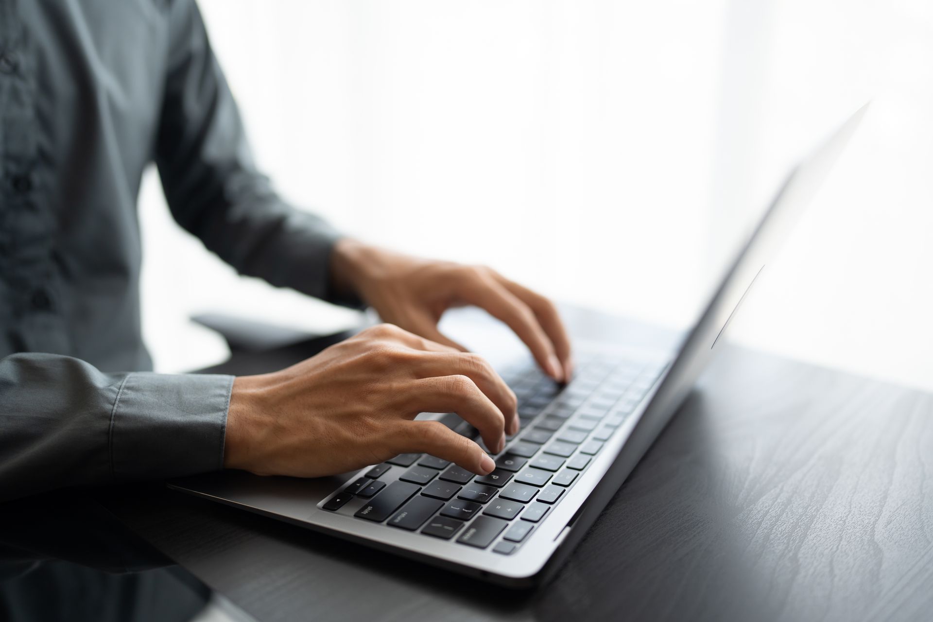 Hands typing on a laptop keyboard at a desk in a bright office setting