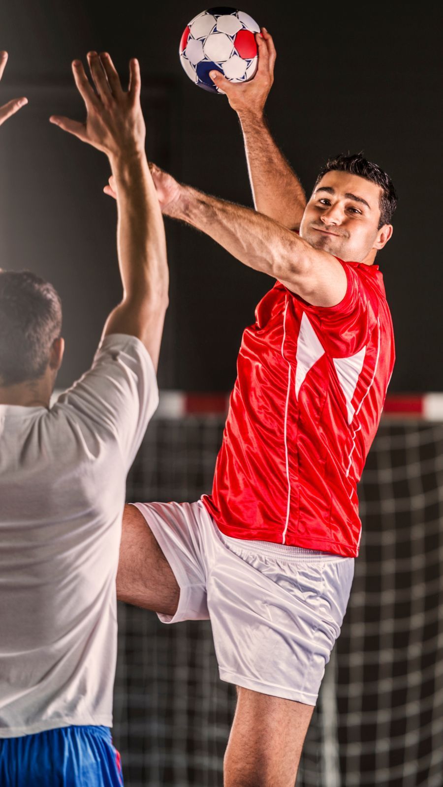 Ein Mann in einem roten Hemd springt in die Luft, um einen Handball zu fangen.