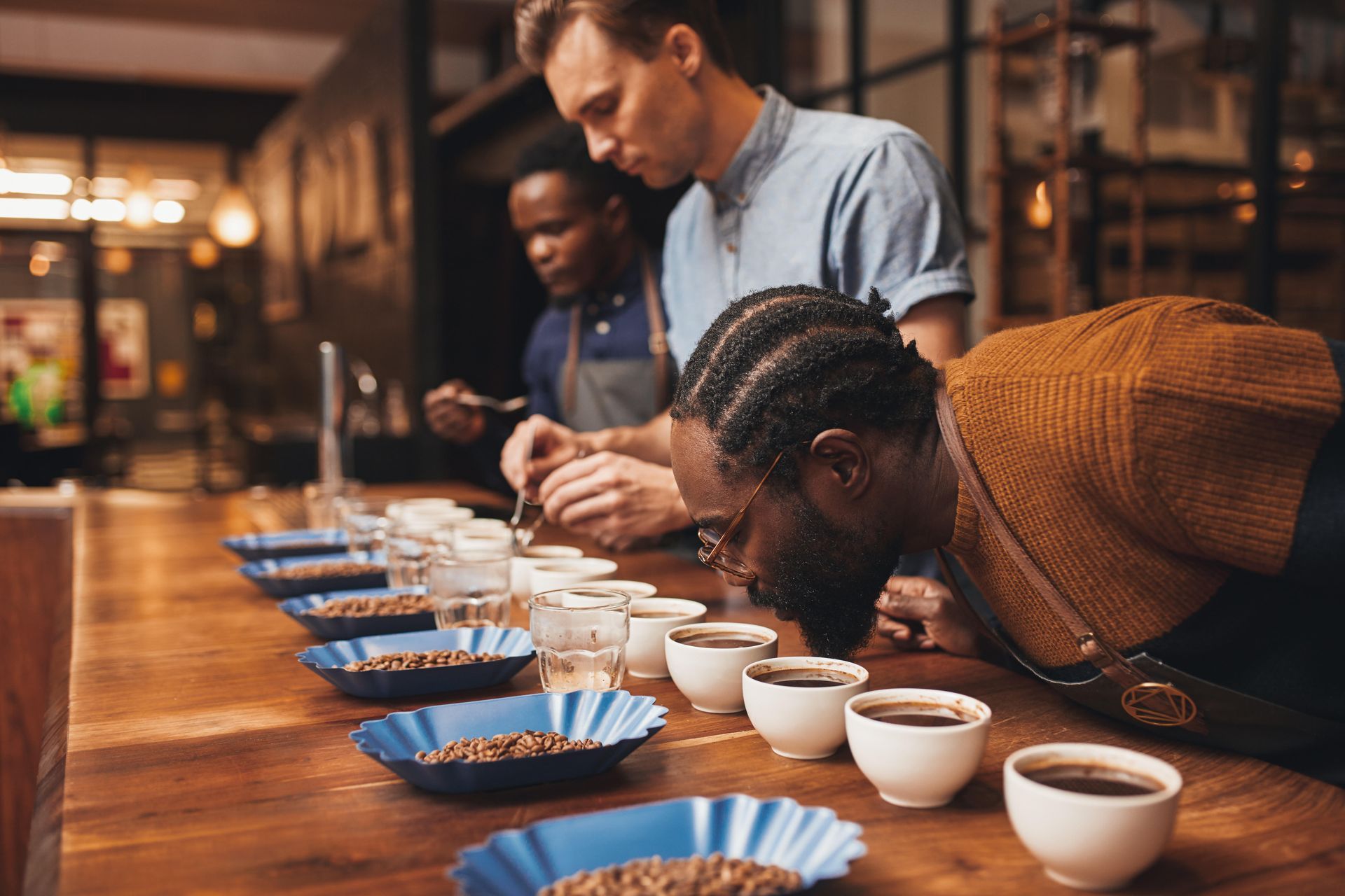 Un grupo de hombres está sentado en una mesa oliendo granos de café.