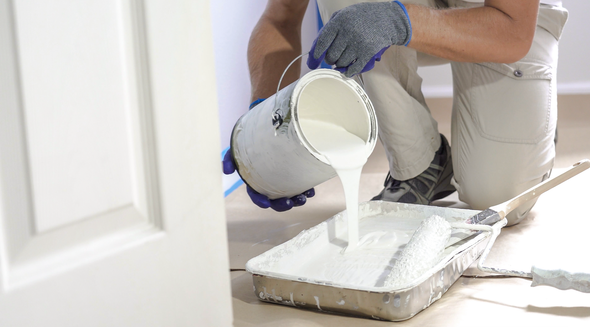 A man is pouring white paint into a tray.