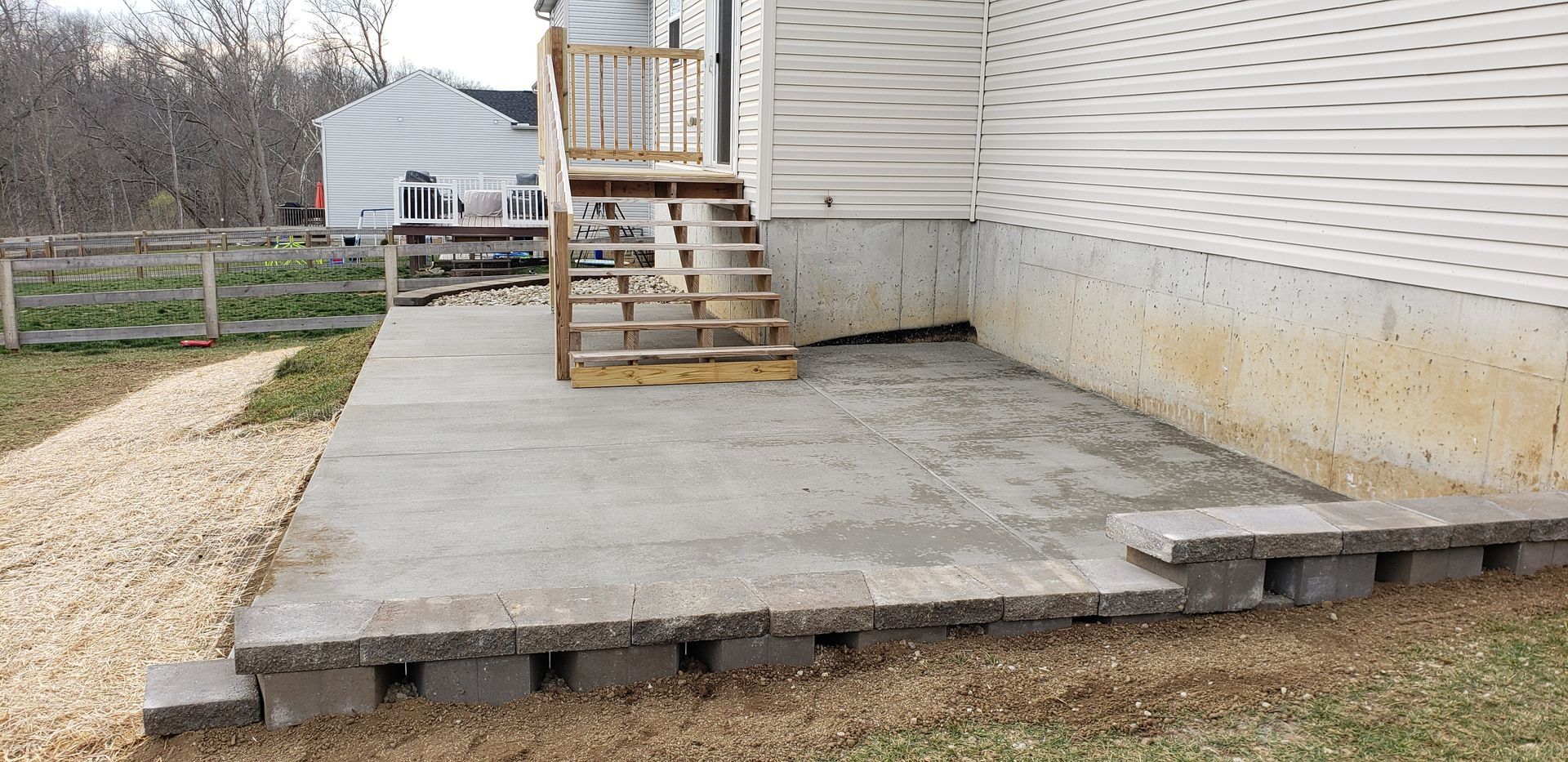 A concrete porch with stairs and a wooden railing on the side of a house.