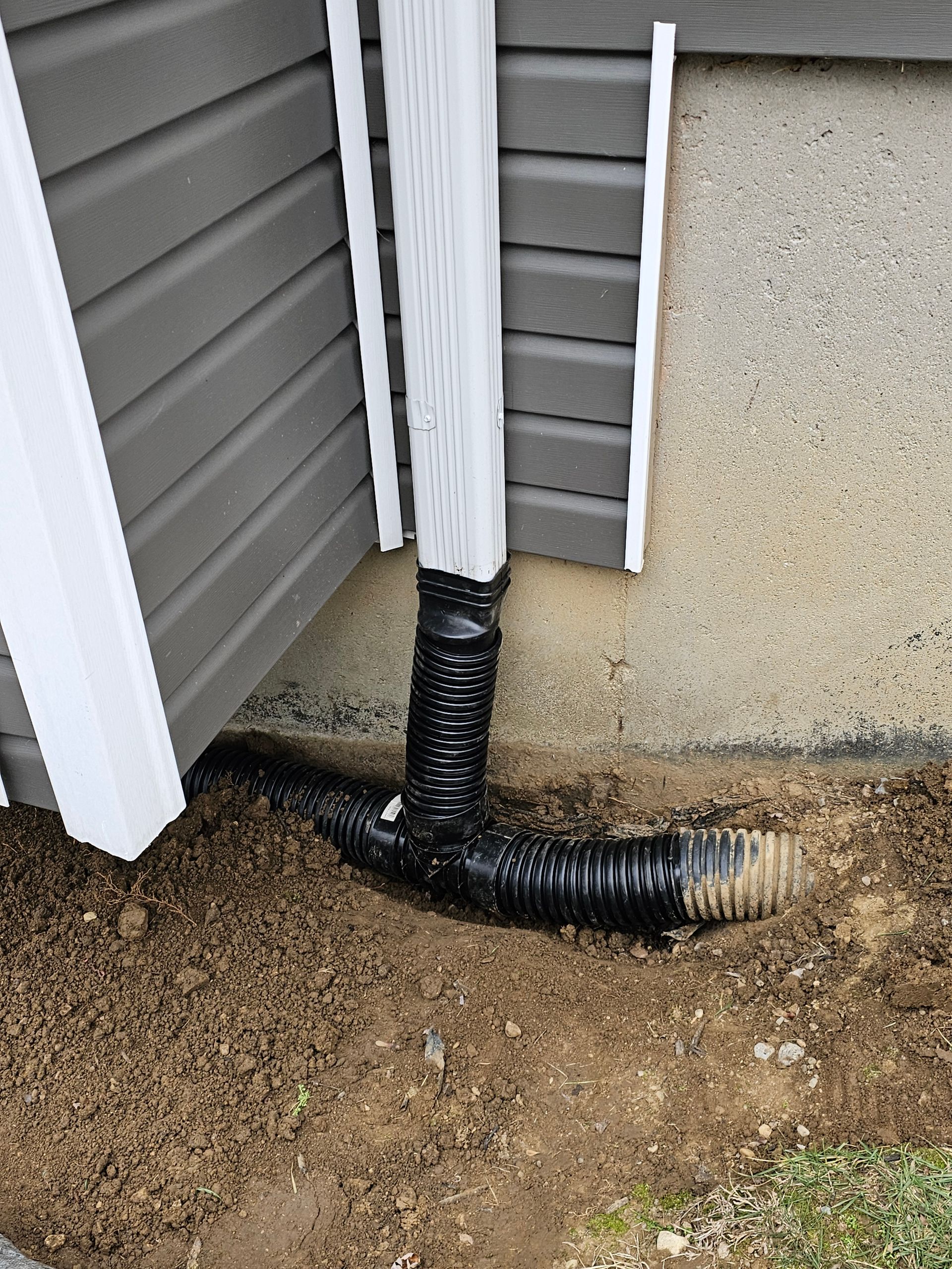 A black drain pipe is sitting in the dirt next to a house.
