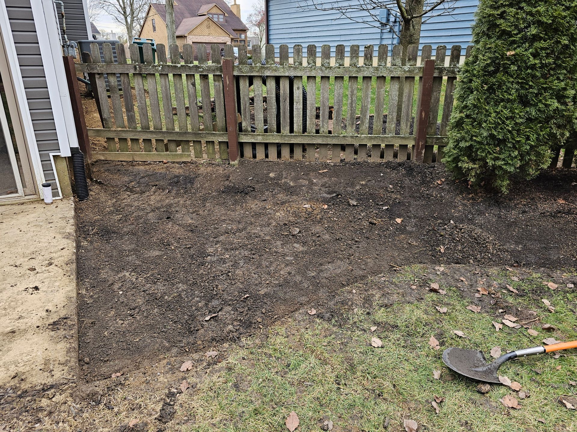 A shovel is sitting in the grass in front of a wooden fence.